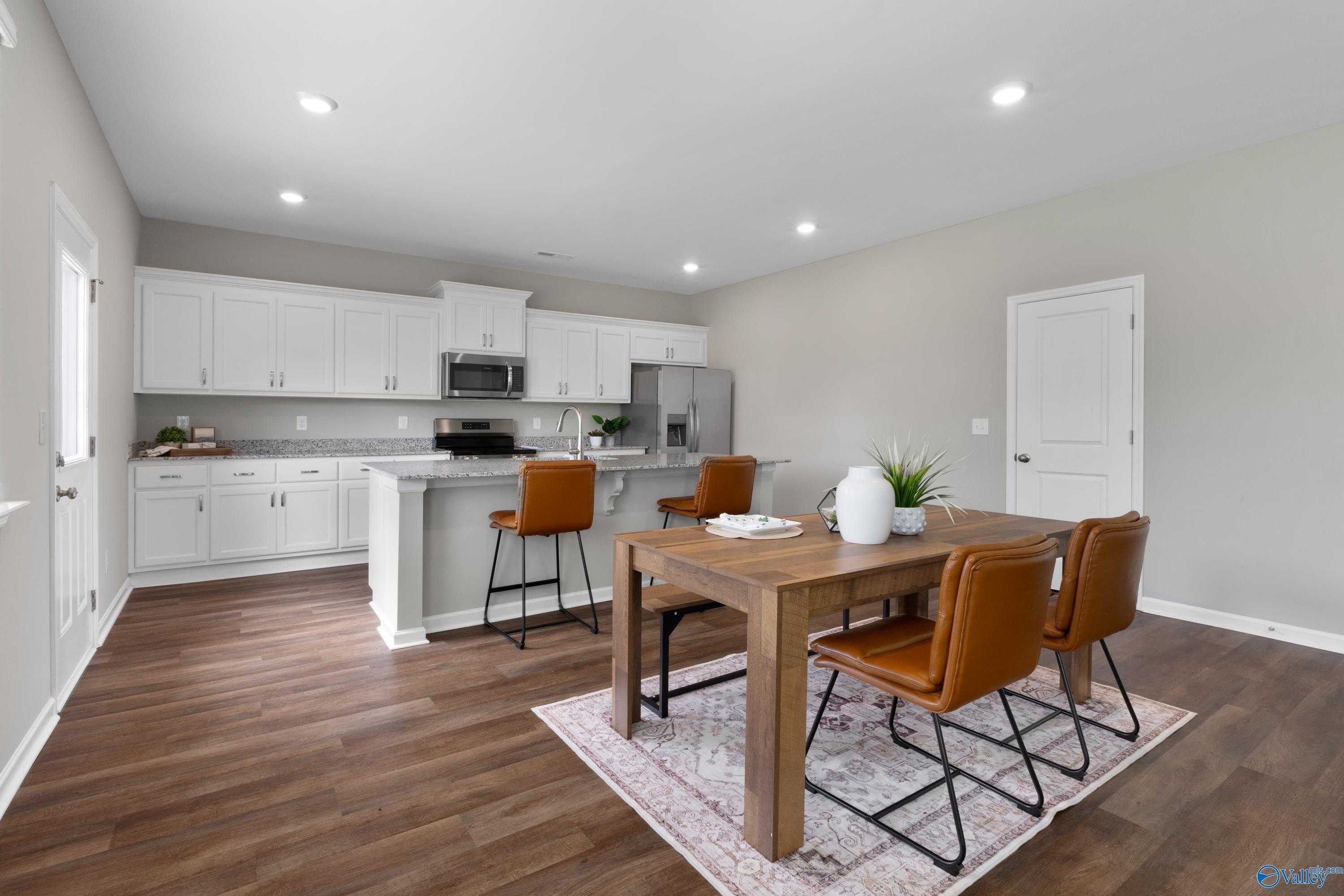 Modern kitchen with white cabinets, stainless appliances, wooden island table, and leather chairs in Evermore Homes The Noble, Madison Alabama