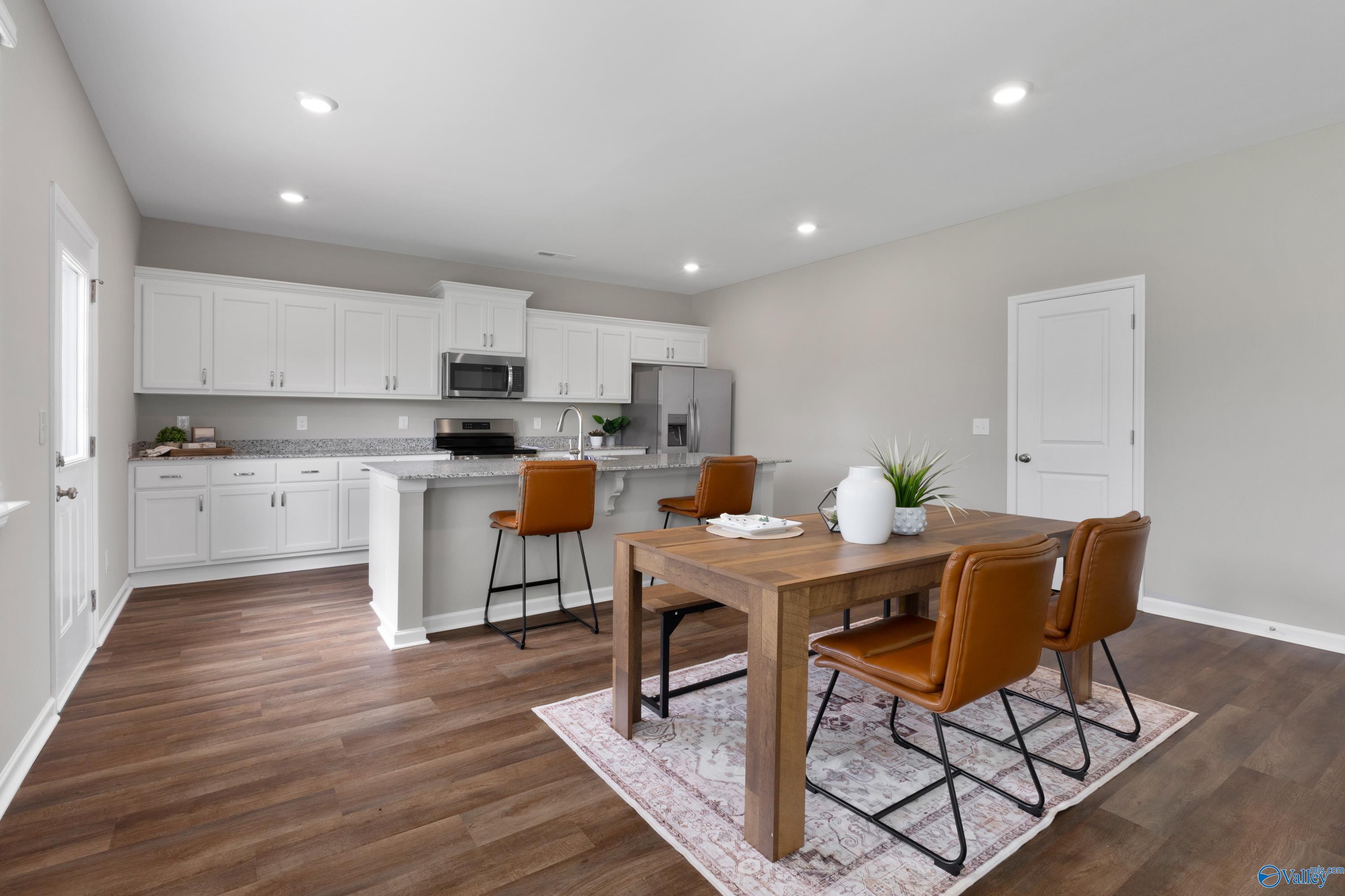 Modern open kitchen with white cabinets, granite island, stainless appliances, and wooden dining table in Davidson Homes The Noble, Madison Alabama