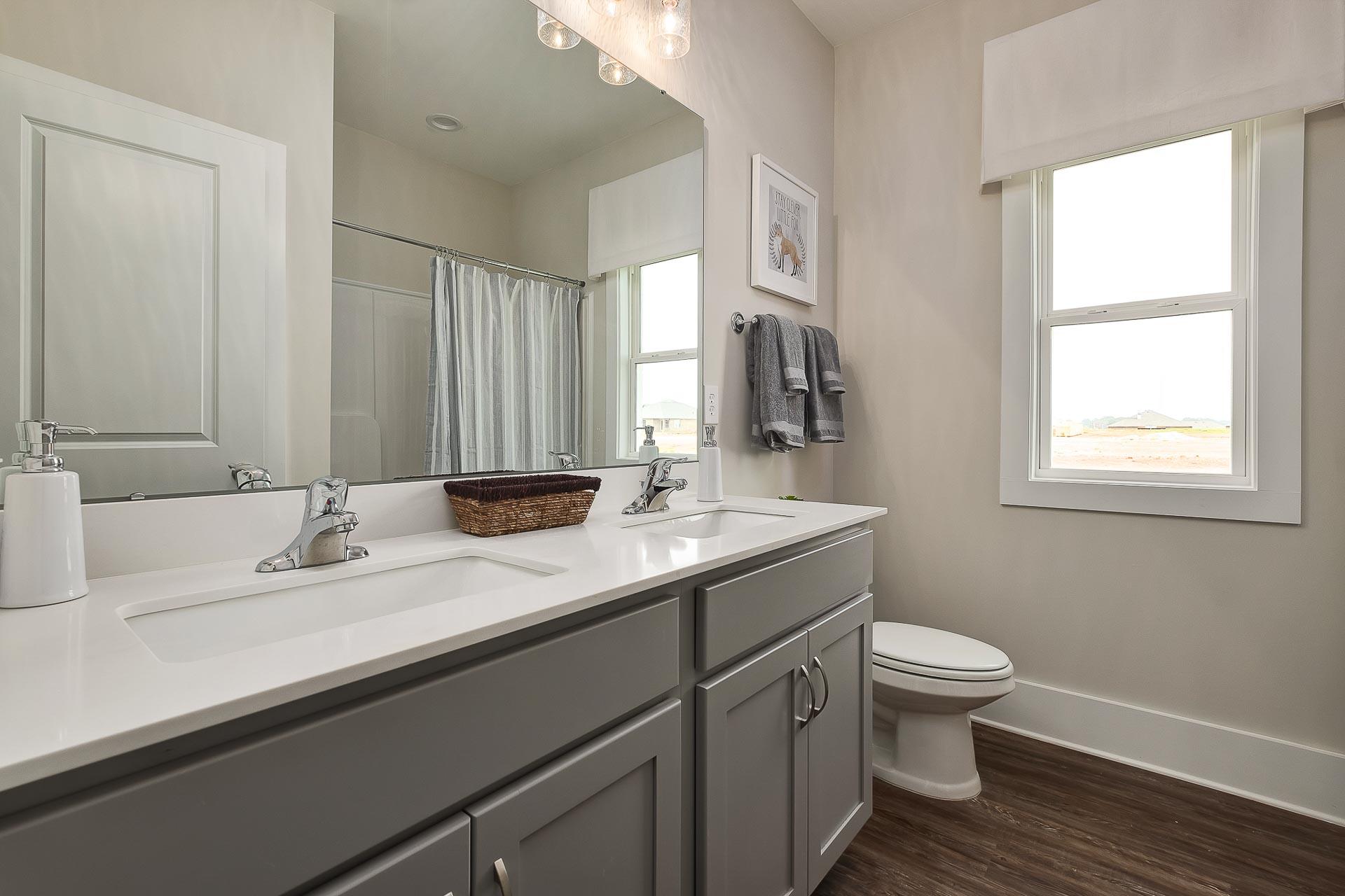 Modern master bathroom in The Everett featuring gray double vanity, white quartz counters, walk-in shower, and window