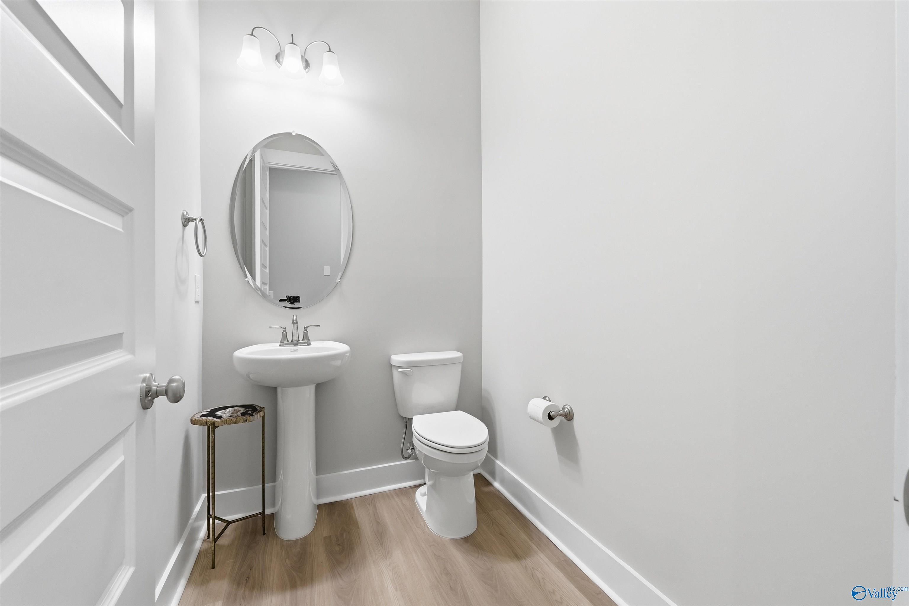 Elegant powder room with pedestal sink, oval mirror, toilet, and agate side table in Evermore Homes The Oxford B, Owens Cross Roads, Alabama