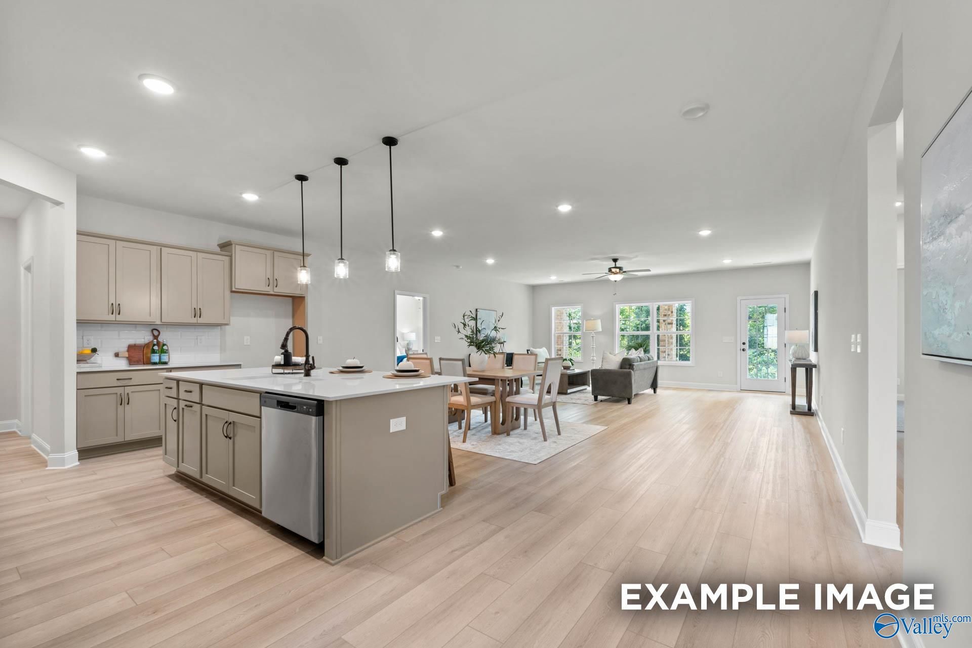 Open-concept kitchen with beige cabinets, island sink, dining table, and living area in The Kirkland by Davidson Homes, Decatur, AL