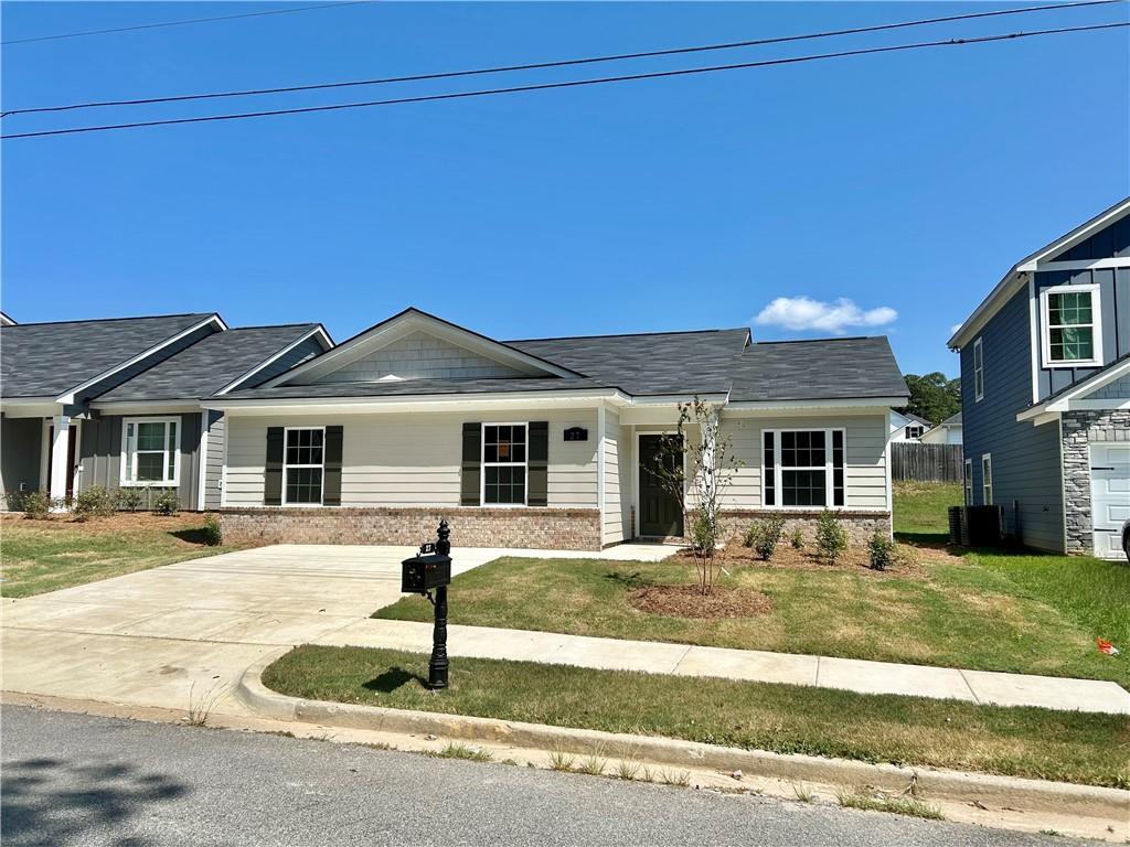Single-story beige home with brick accents, dark shingle roof, driveway, and landscaped yard in Summer Vineyard, Phenix City, Alabama