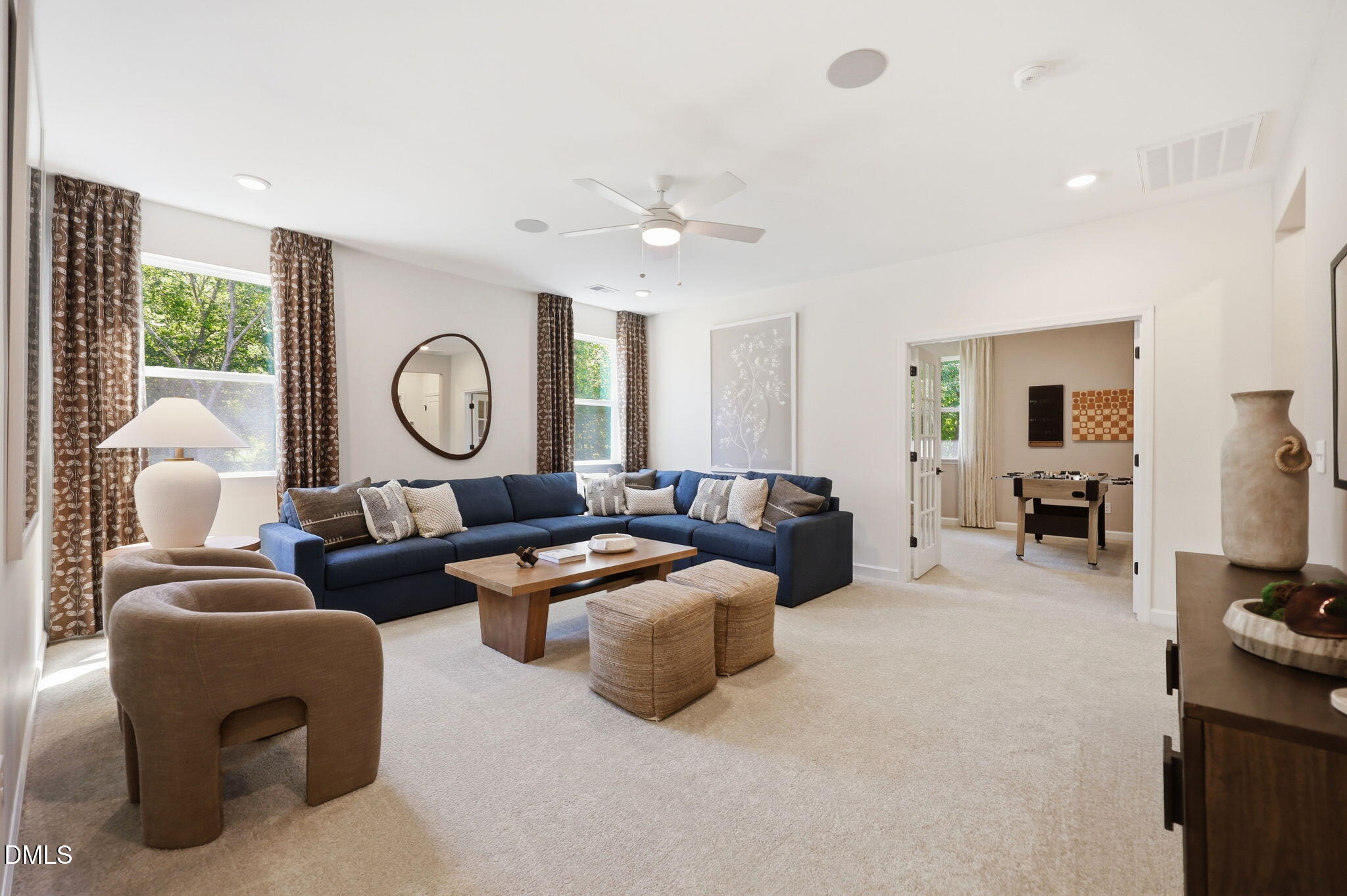 Spacious living room with blue sectional and game room in The Aspen B floor plan by Davidson Homes in Wendell, North Carolina.