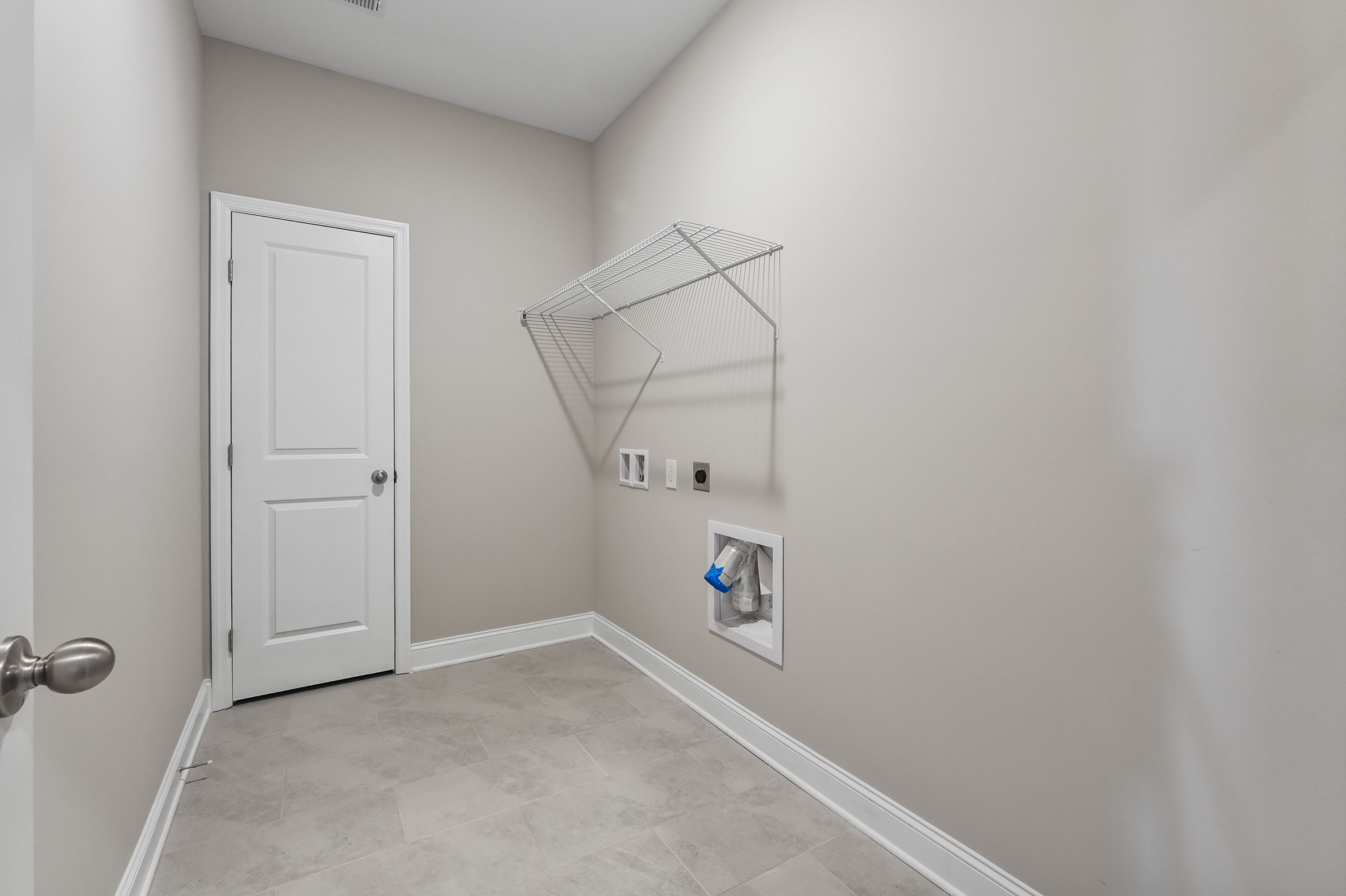 Spacious laundry room in The Valencia Davidson Homes design featuring white door, beige walls, hanging rod, washer-dryer hookups, tiled floor