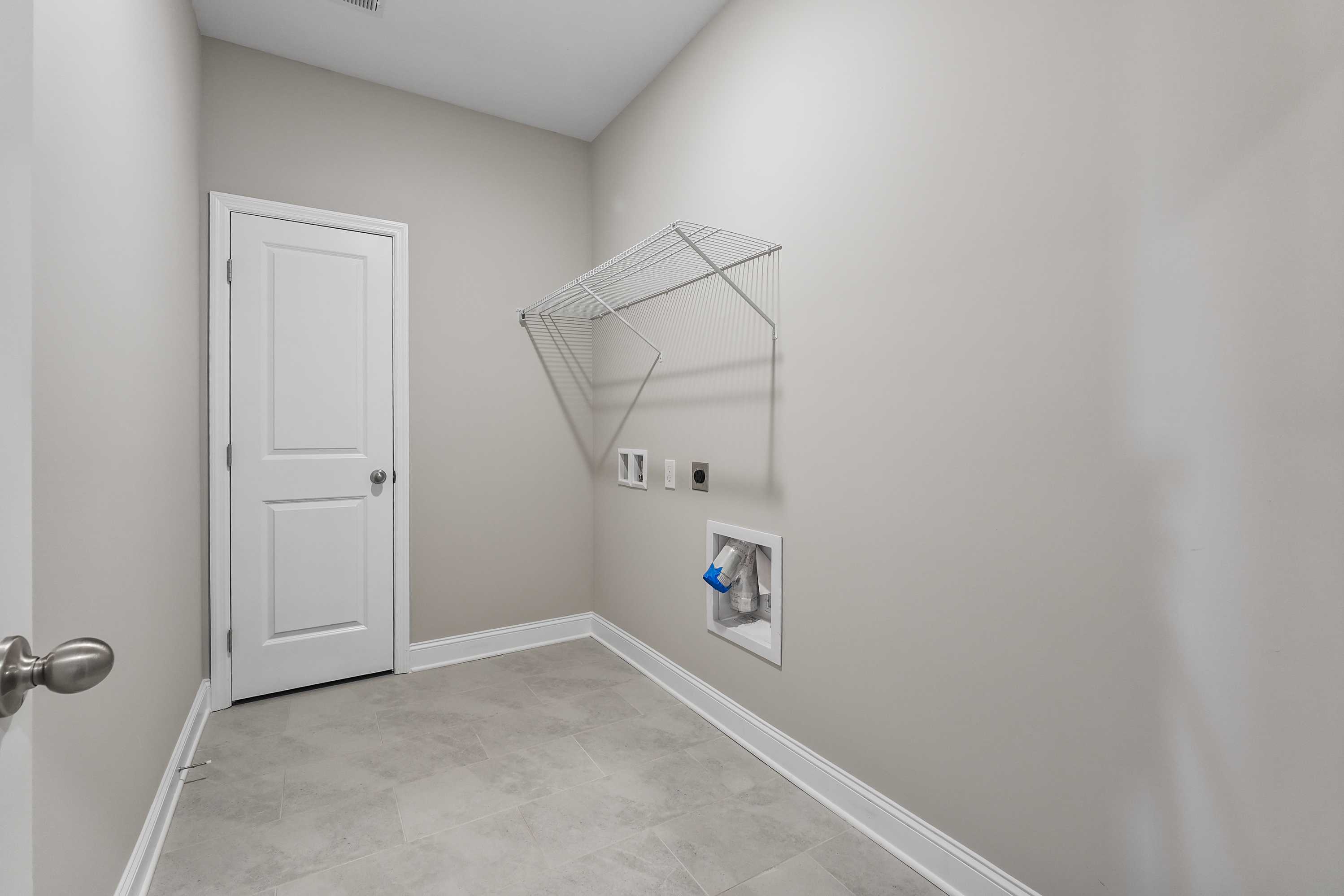 Spacious laundry room in The Valencia Davidson Homes design featuring white door, beige walls, hanging rod, washer-dryer hookups, tiled floor