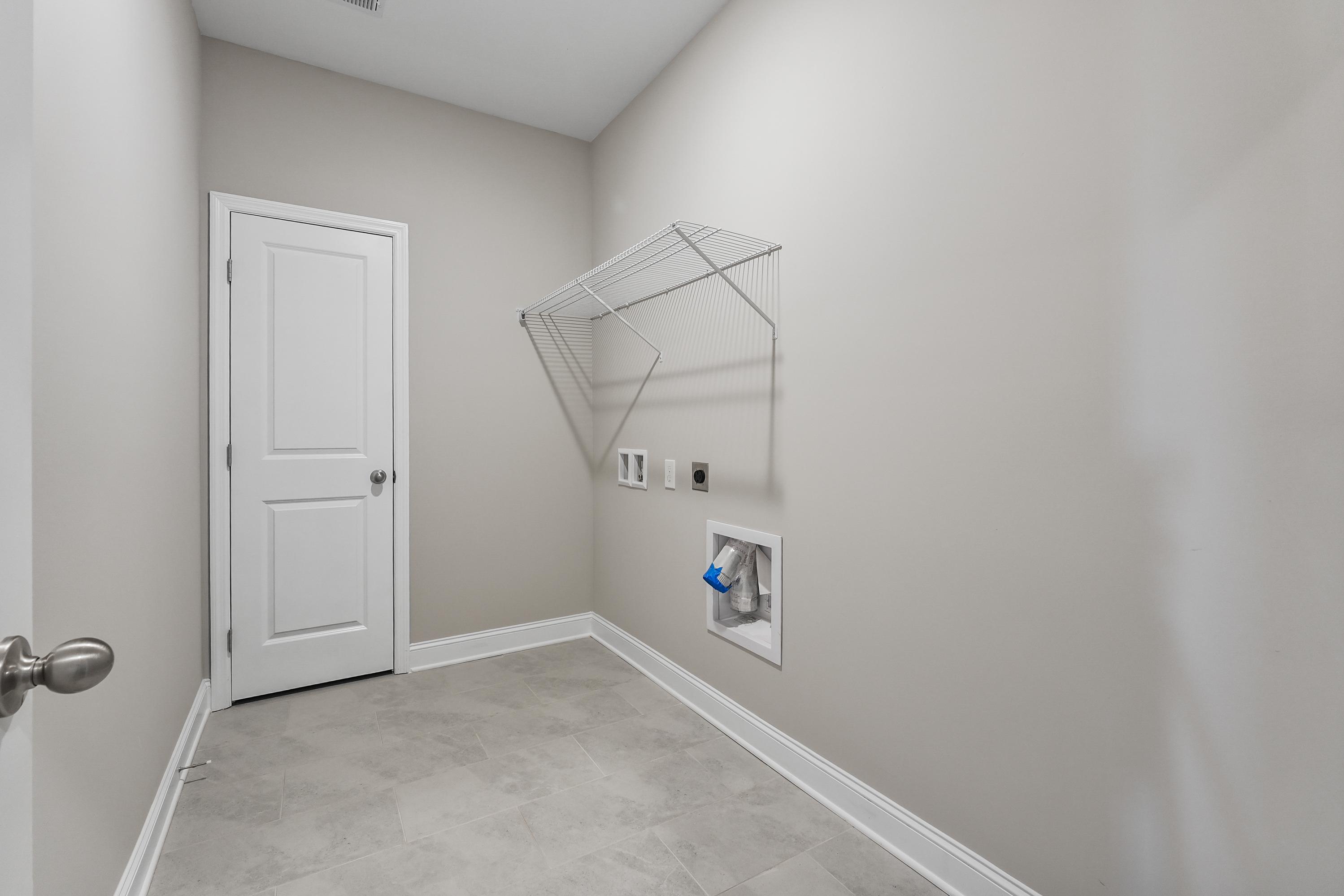 Spacious laundry room in The Valencia Davidson Homes design featuring white door, beige walls, hanging rod, washer-dryer hookups, tiled floor