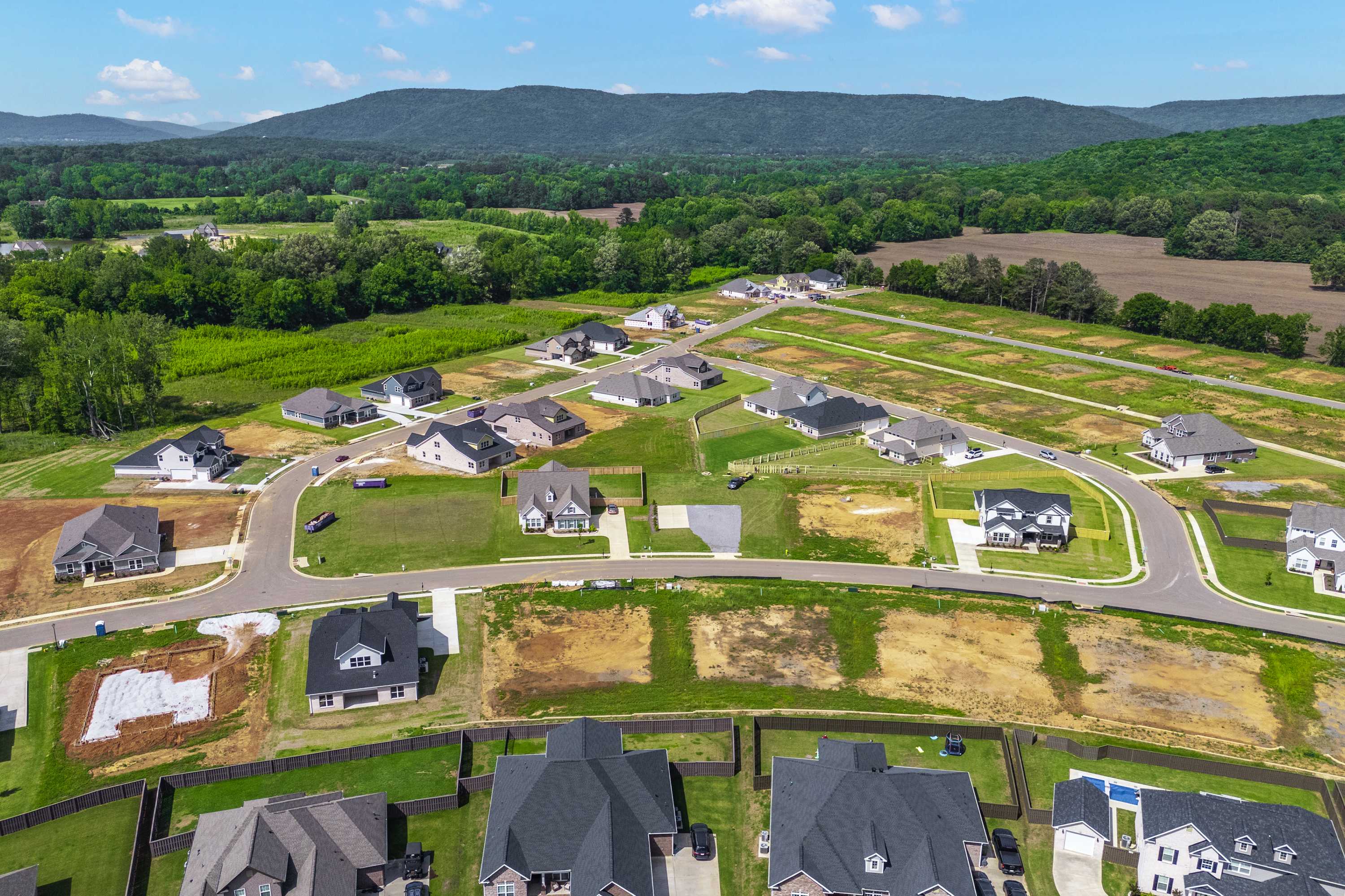 Aerial view of developing homes in The Meadows at Hampton Cove, Owens Cross Roads Alabama amid green fields and mountain backdrop