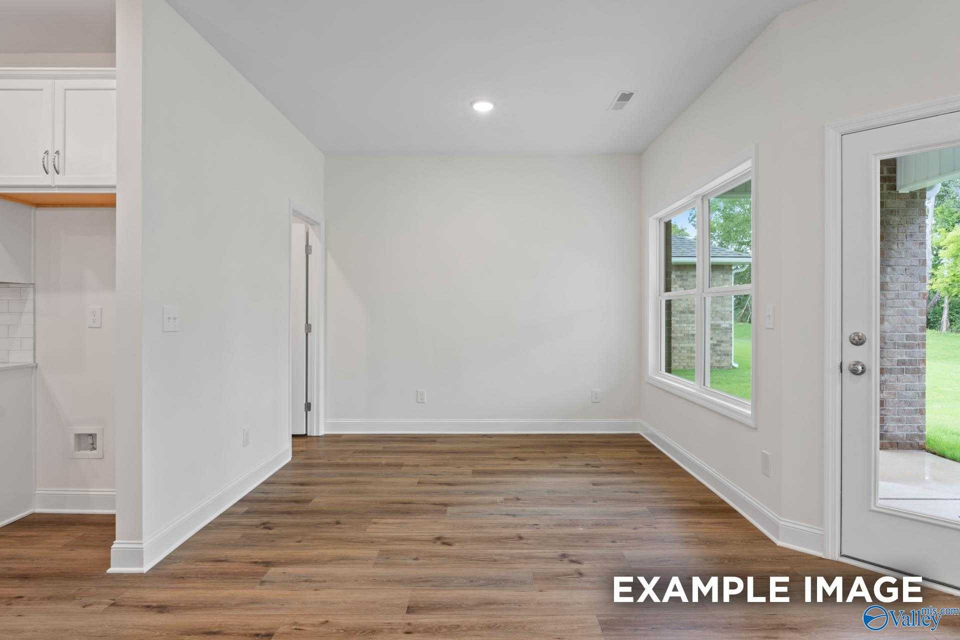 Bright living room with hardwood floors, white walls, and large windows to backyard in Davidson Homes The Daphne D, Athens, Alabama