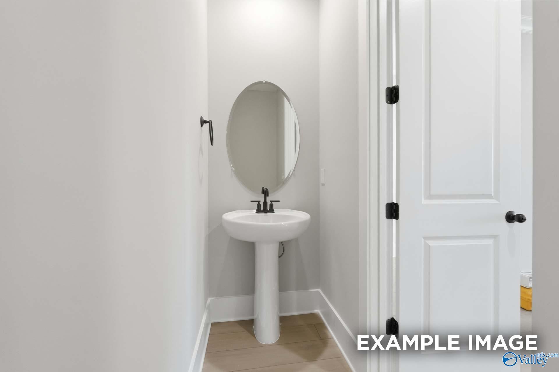 Elegant powder room with white pedestal sink and round mirror in Davidson Homes The Emory, Hollon Meadow, Decatur, Alabama