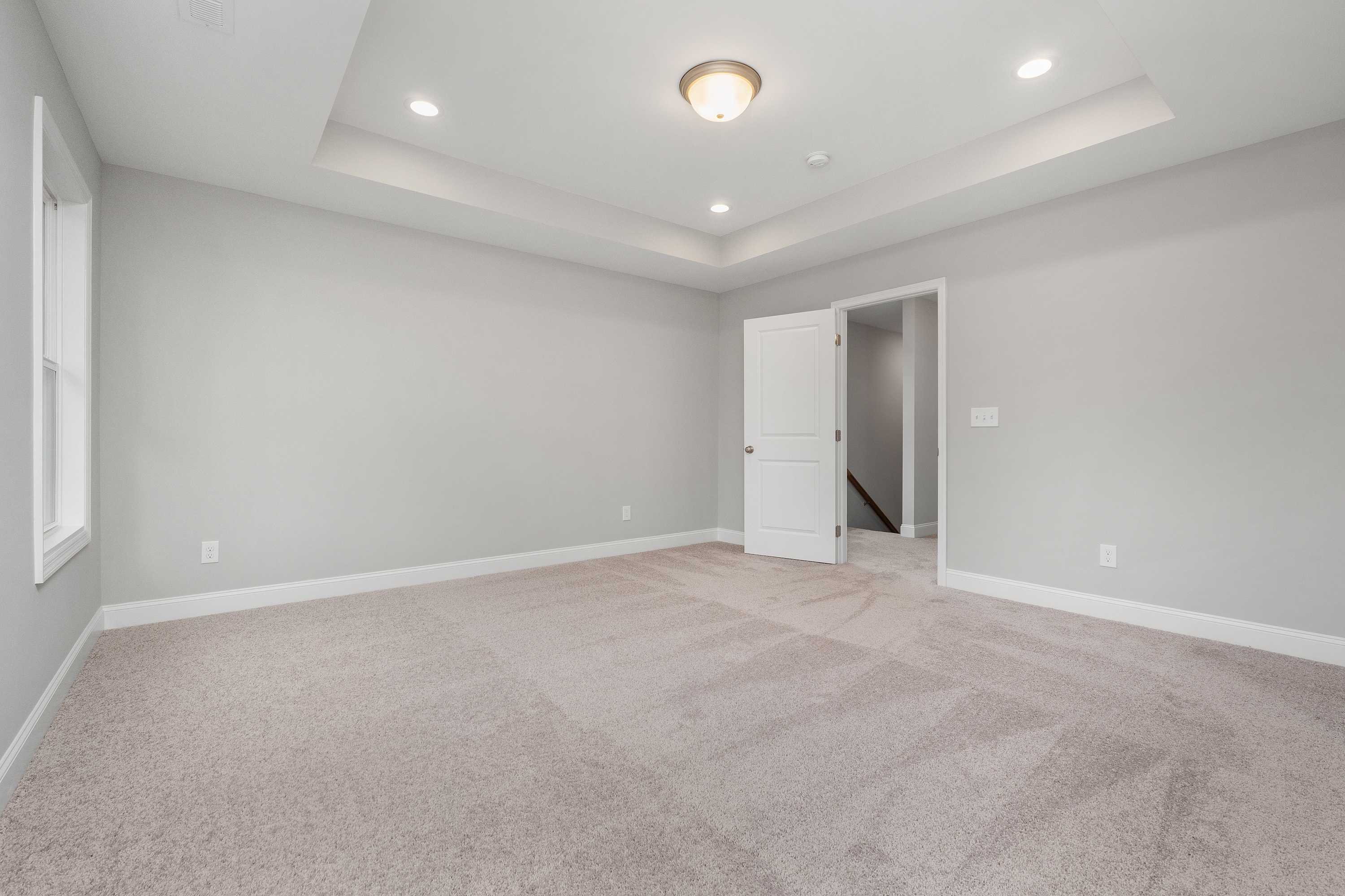 Spacious master bedroom in The Aiken home design with light gray walls, beige carpet, open white door, and recessed ceiling lights
