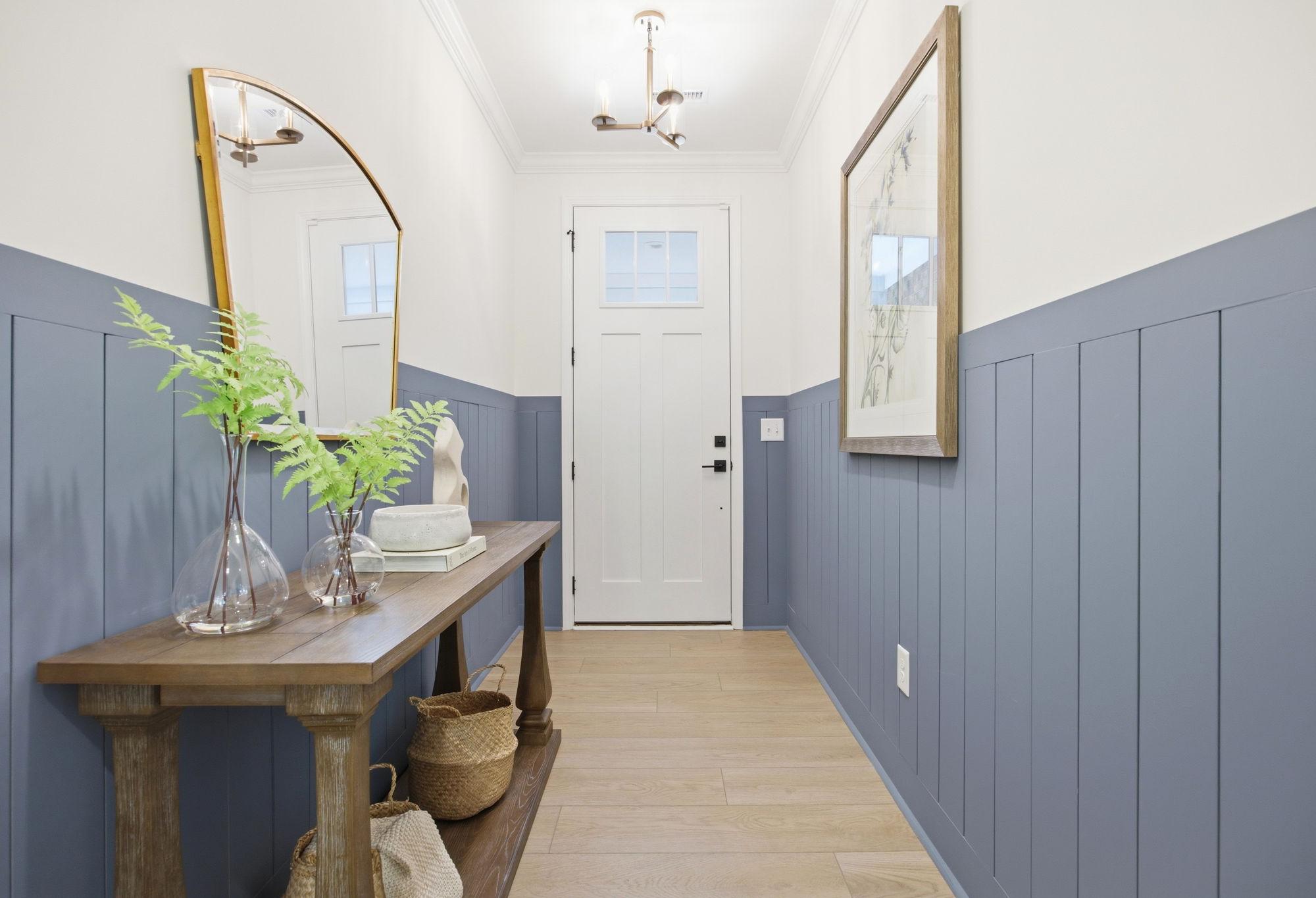 Bright entryway in The Ashport featuring blue board and batten wainscoting, wood console table, and modern lighting.