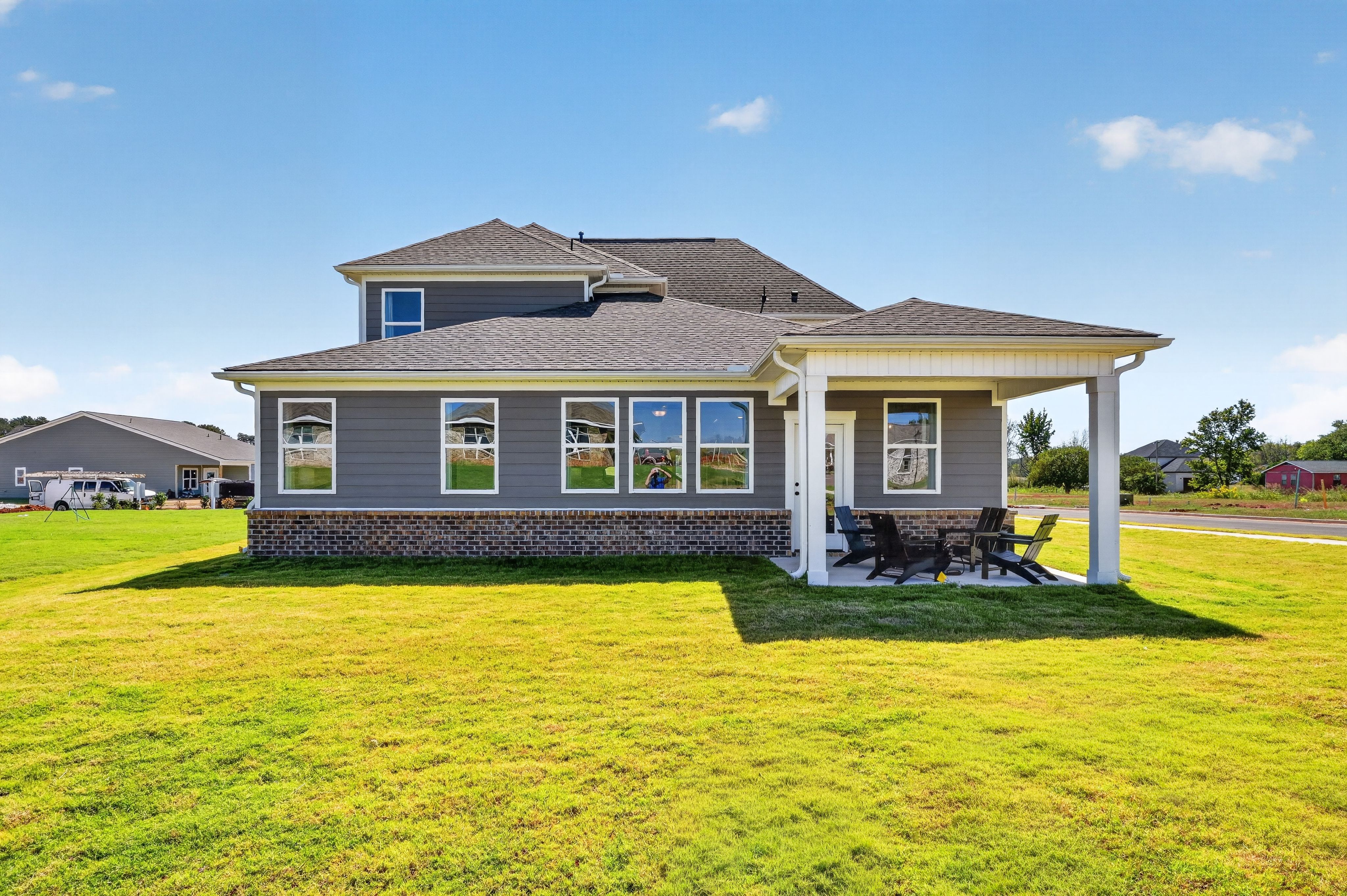 Rear exterior of a gray two-story home with covered patio and seating at Evergreen Mill by Davidson Homes in Madison, Alabama