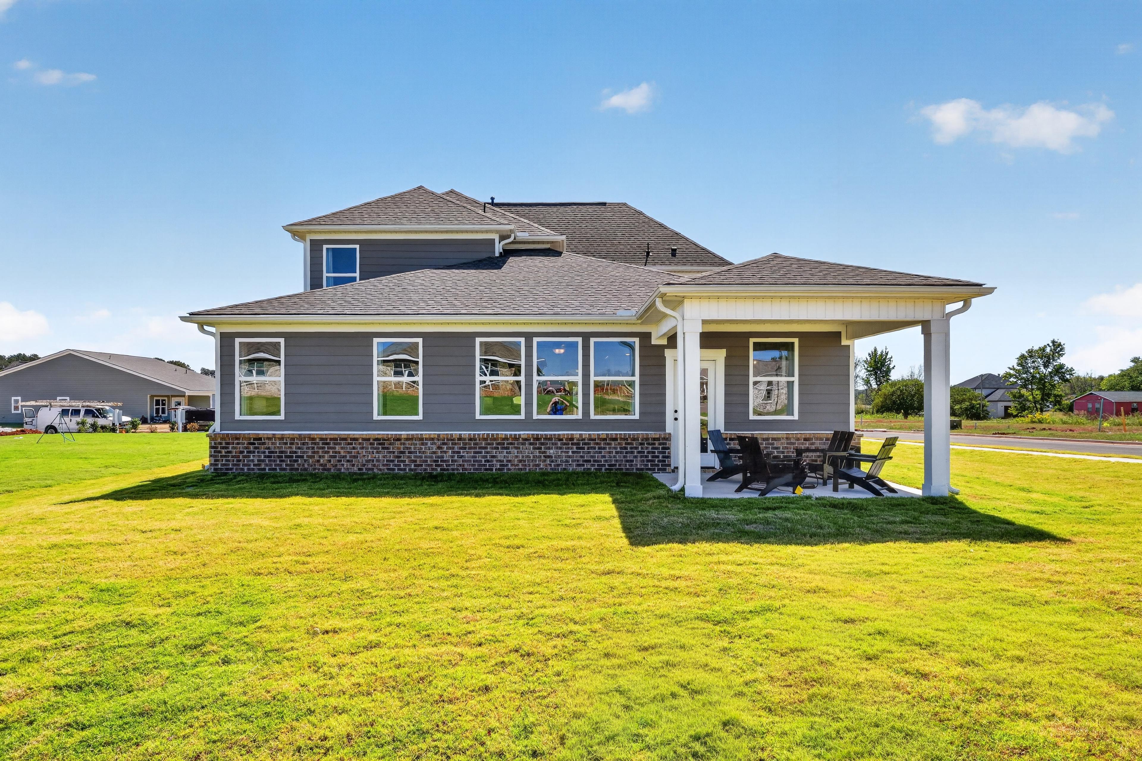 Rear exterior of a gray two-story home with covered patio and seating at Evergreen Mill by Davidson Homes in Madison, Alabama