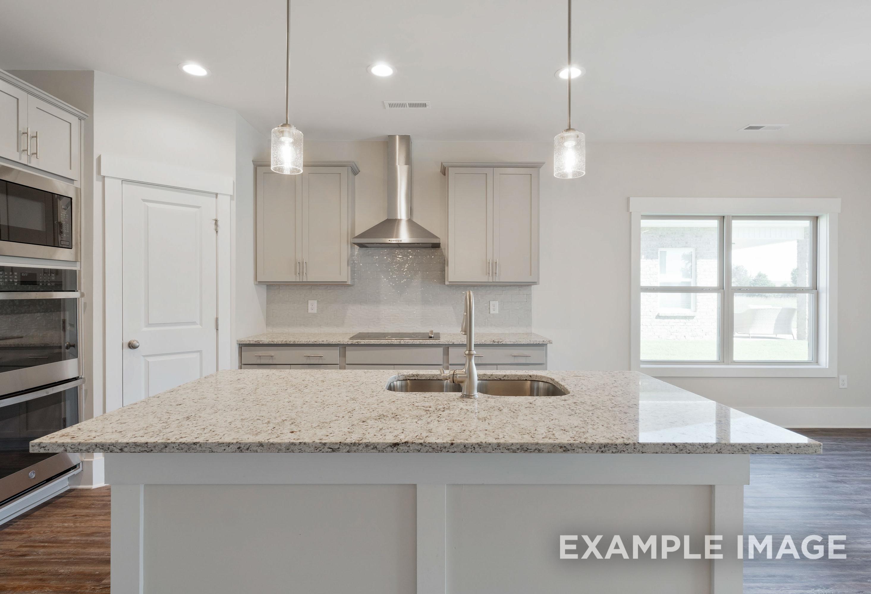 Modern kitchen in The Richmond D featuring a large granite island, stainless steel appliances, and sleek cabinetry.
