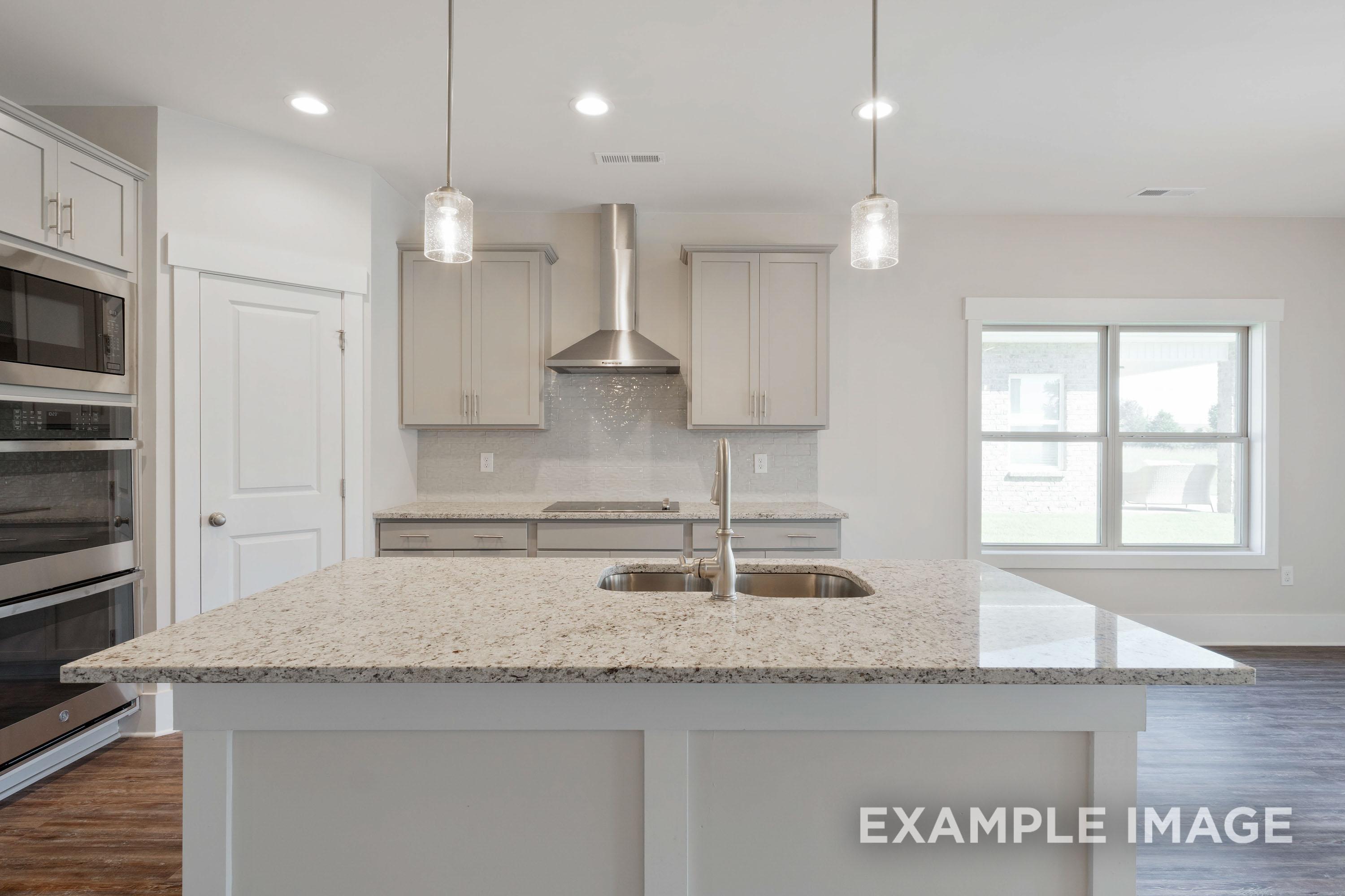 Modern kitchen in The Richmond D featuring a large granite island, stainless steel appliances, and sleek cabinetry.