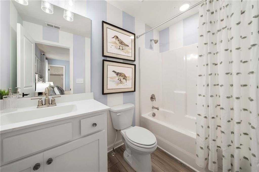 Bright bathroom with blue striped walls, framed bird art, white tub, vanity, and toilet in Davidson Homes The Hickory B, Riverwood, Dallas, Georgia