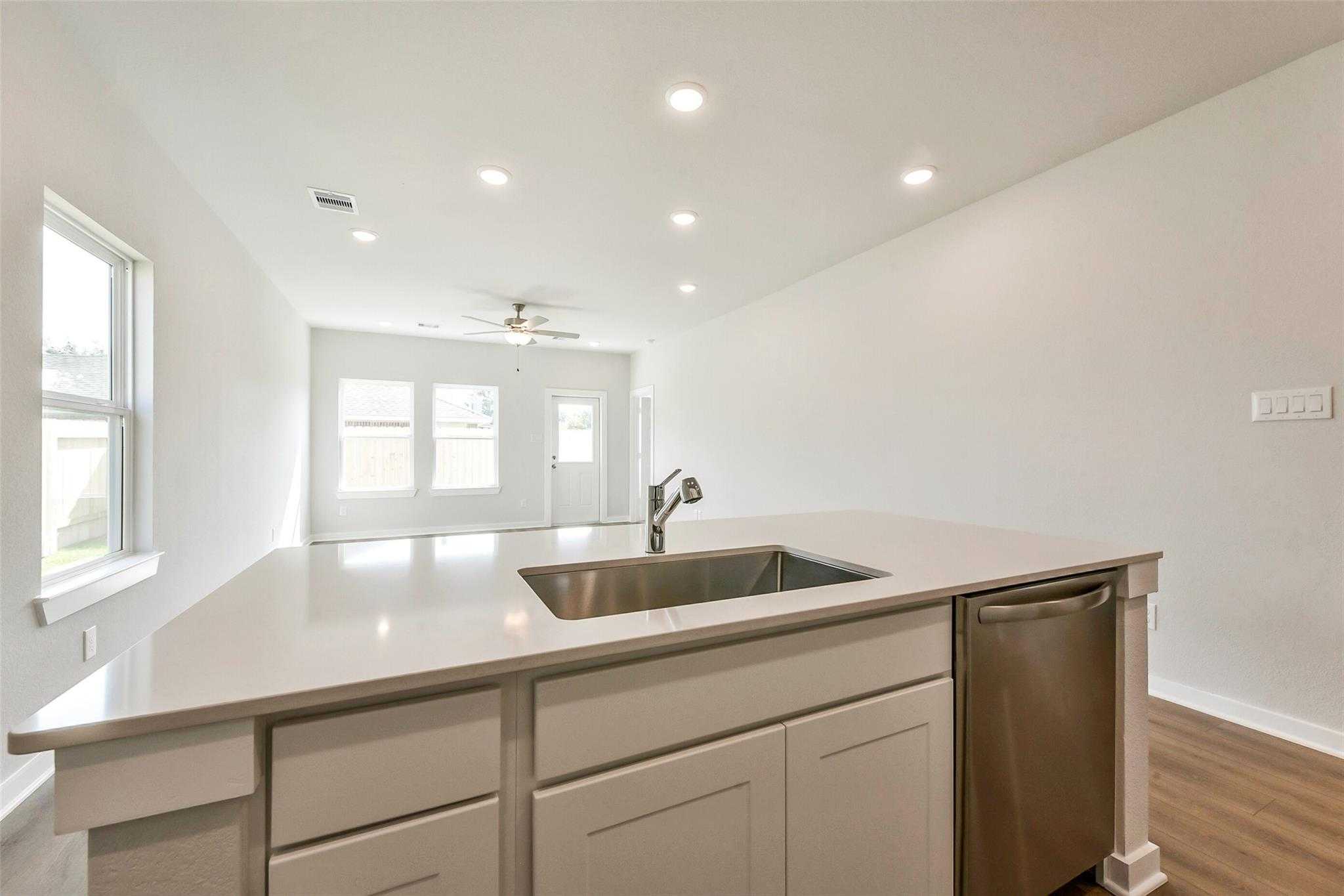 Modern open-concept kitchen with white quartz island, stainless sink, dishwasher, and ceiling fan in The Comal G by Davidson Homes, Dayton TX