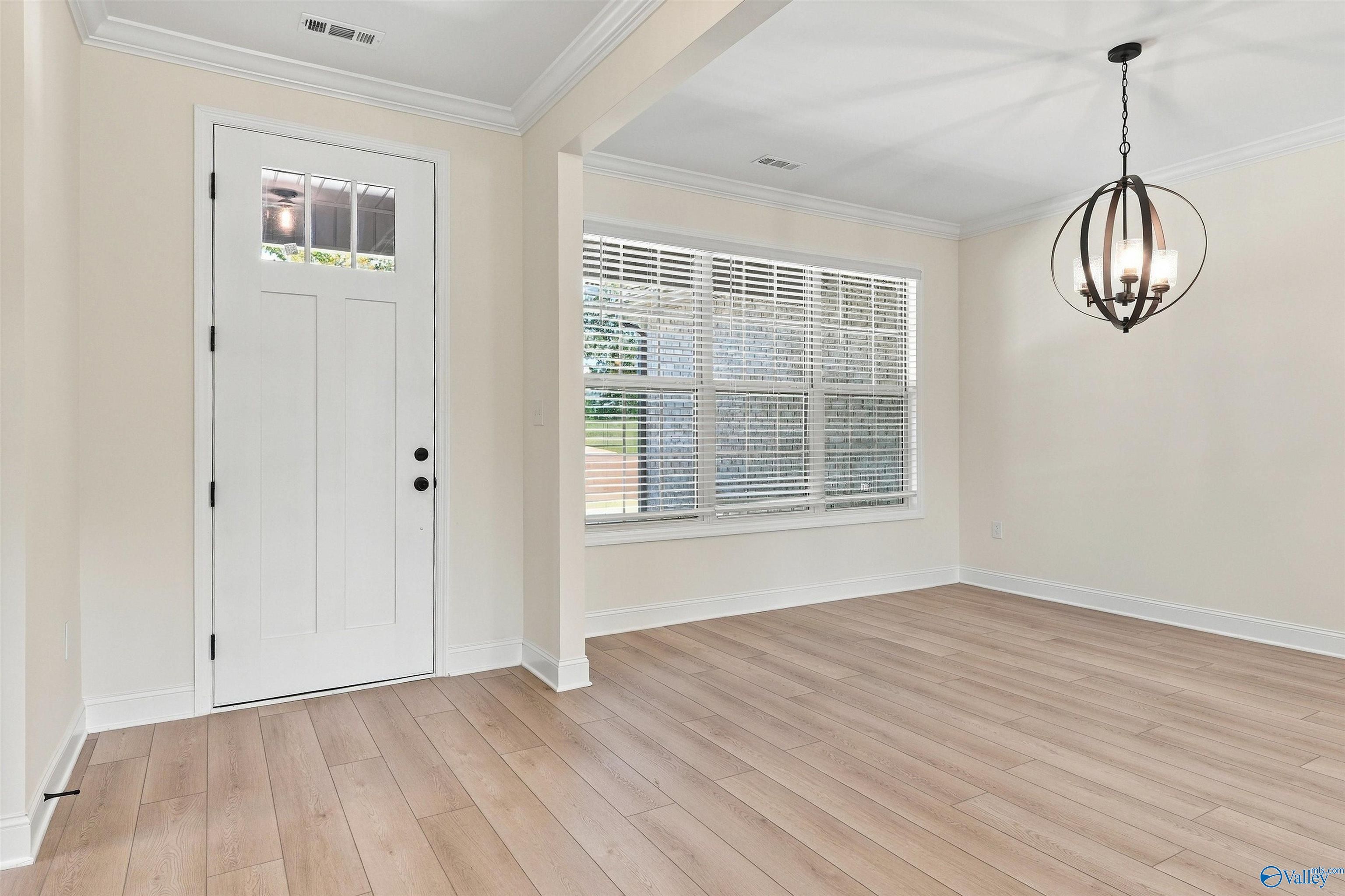 Bright entryway with white front door, wood-look flooring, and orb chandelier in The Valencia floor plan, Huntsville, Alabama
