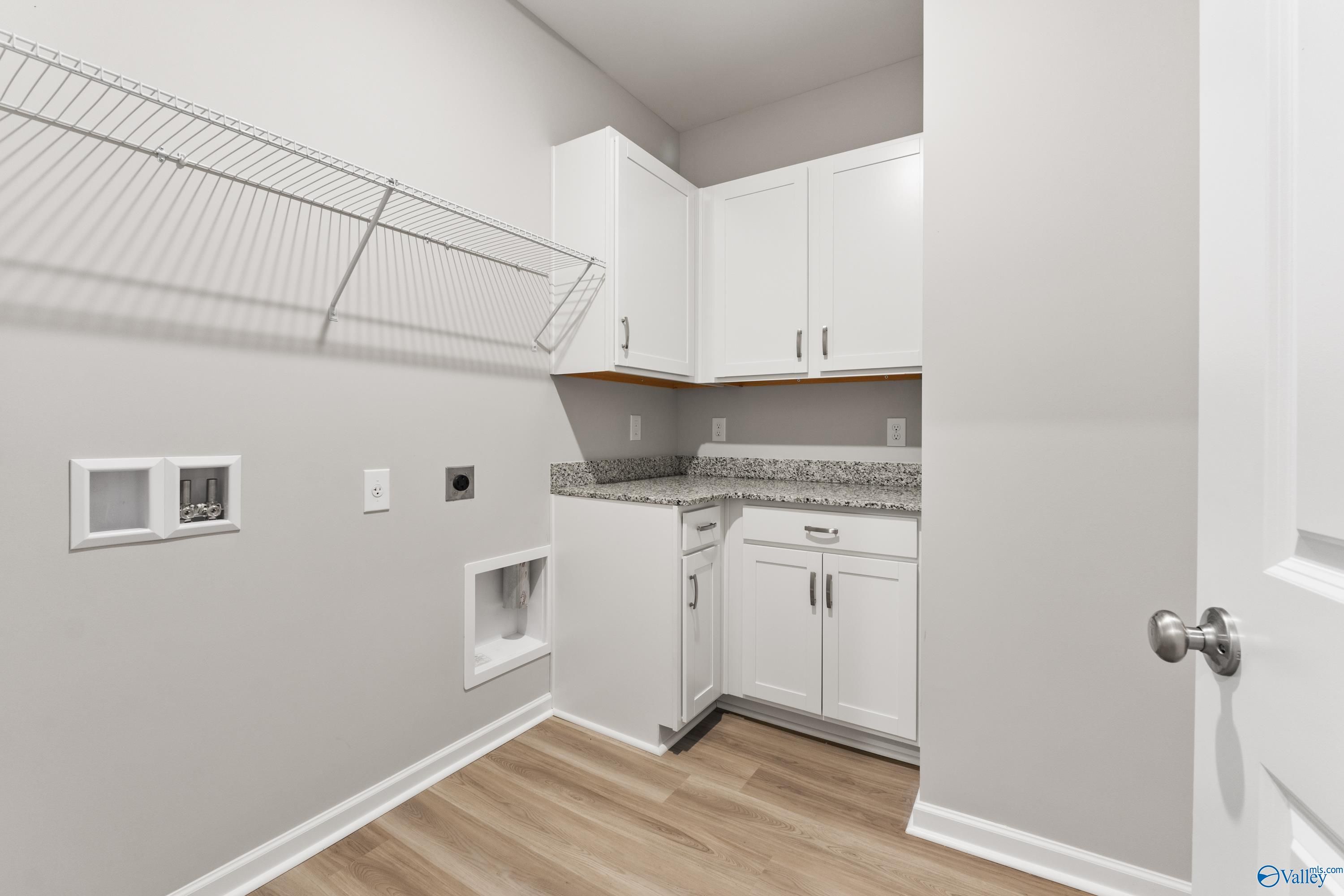 Modern laundry room featuring white shaker cabinets, granite countertop, wire shelving, and washer-dryer hookups in Davidson Homes The Phoenix, Hazel Green, AL