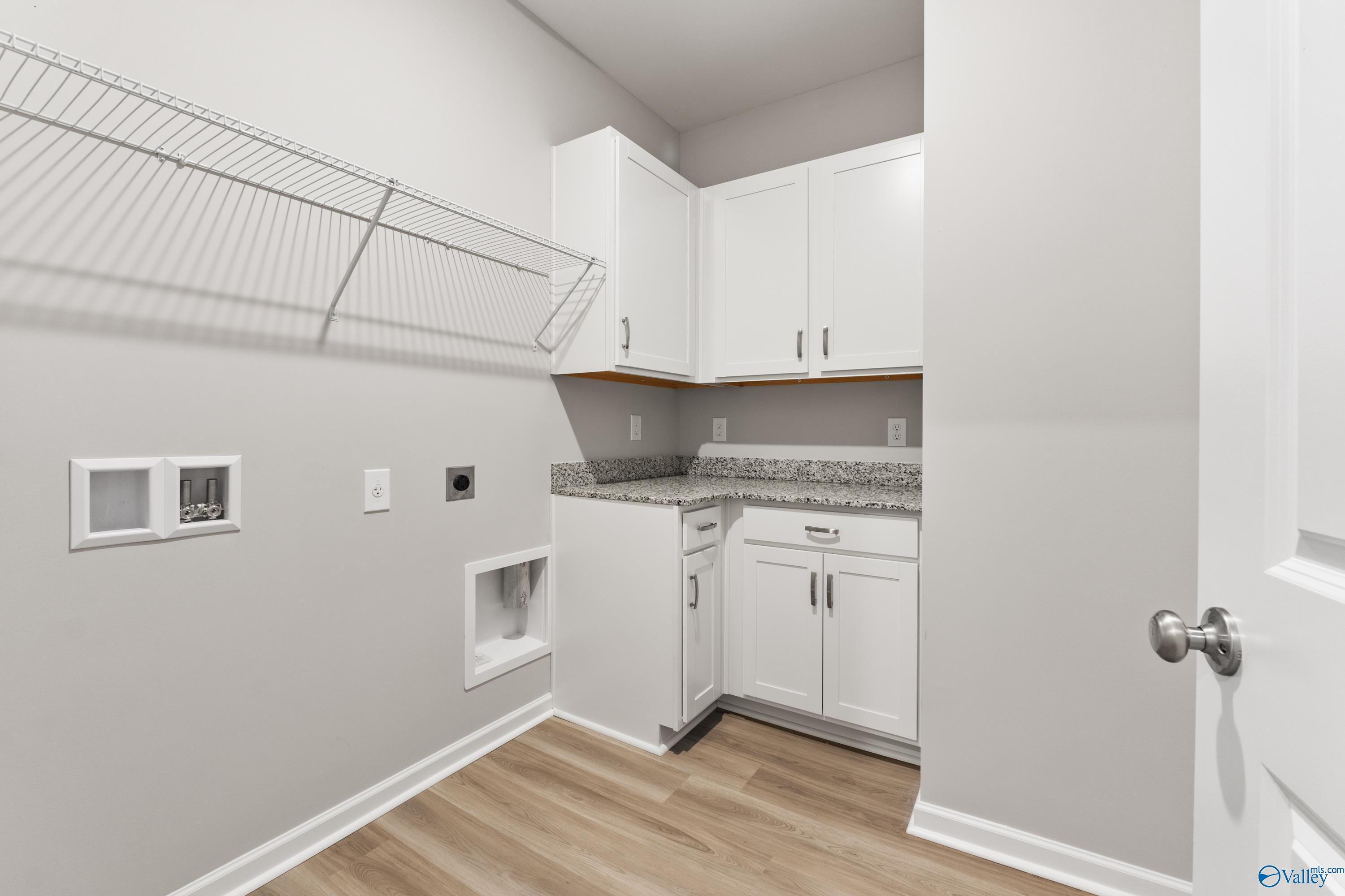 Modern laundry room featuring white shaker cabinets, granite countertop, wire shelving, and washer-dryer hookups in Davidson Homes The Phoenix, Hazel Green, AL