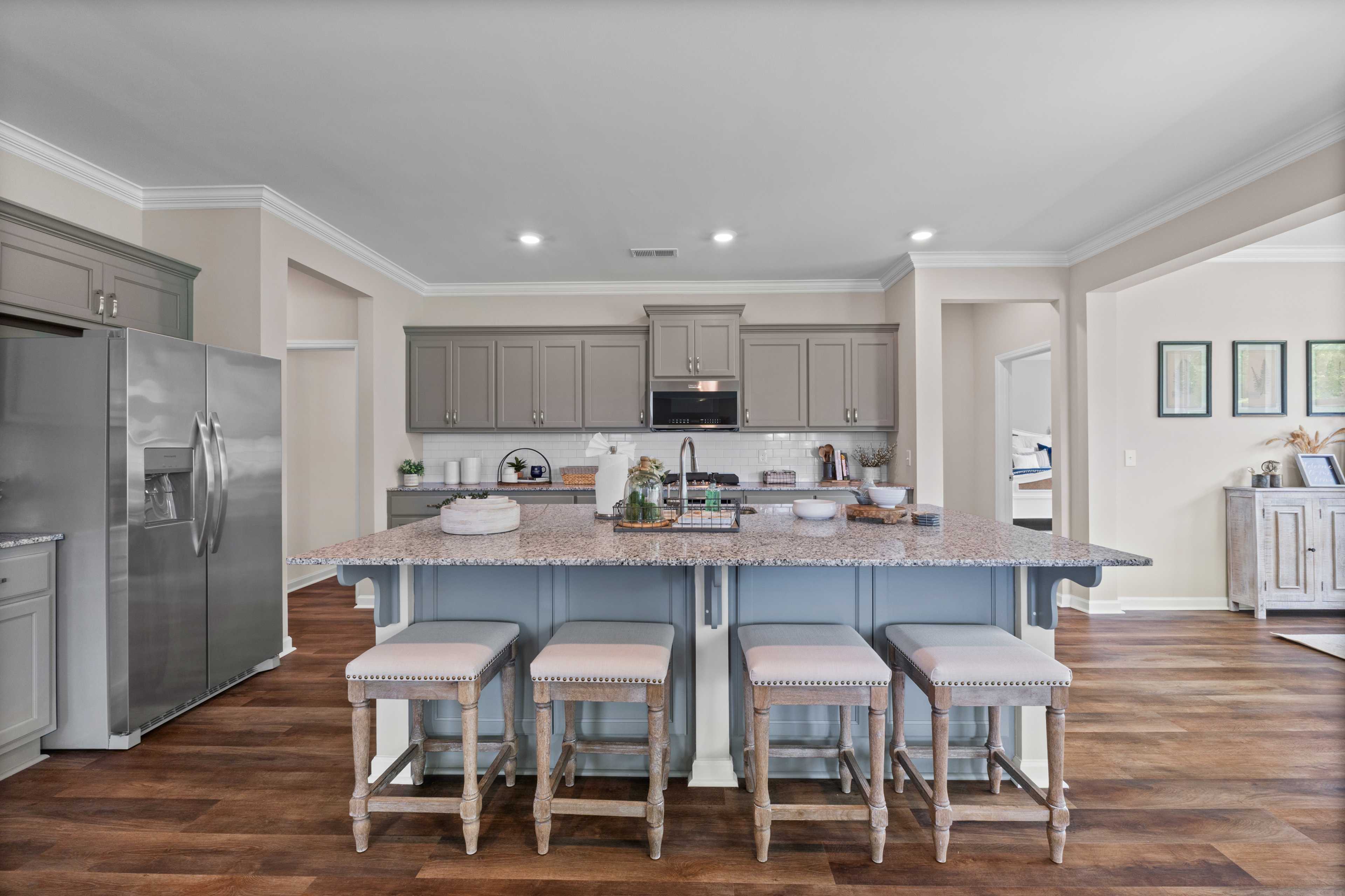 Spacious modern kitchen at Riverton Preserve in Huntsville AL with gray shaker cabinets, stainless steel appliances, blue quartz island and upholstered bar stools