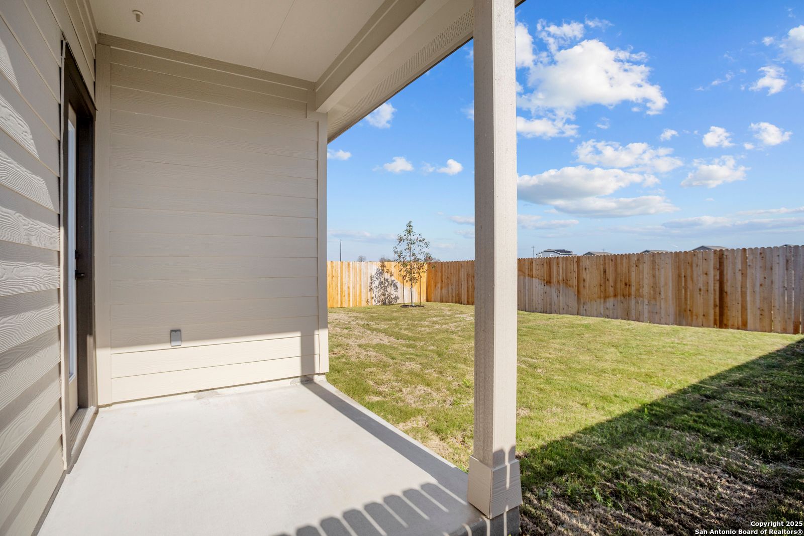 Covered back patio overlooking grassy backyard with wooden fence in Davidson Homes The Daphne H, Hannah Heights, Seguin, Texas