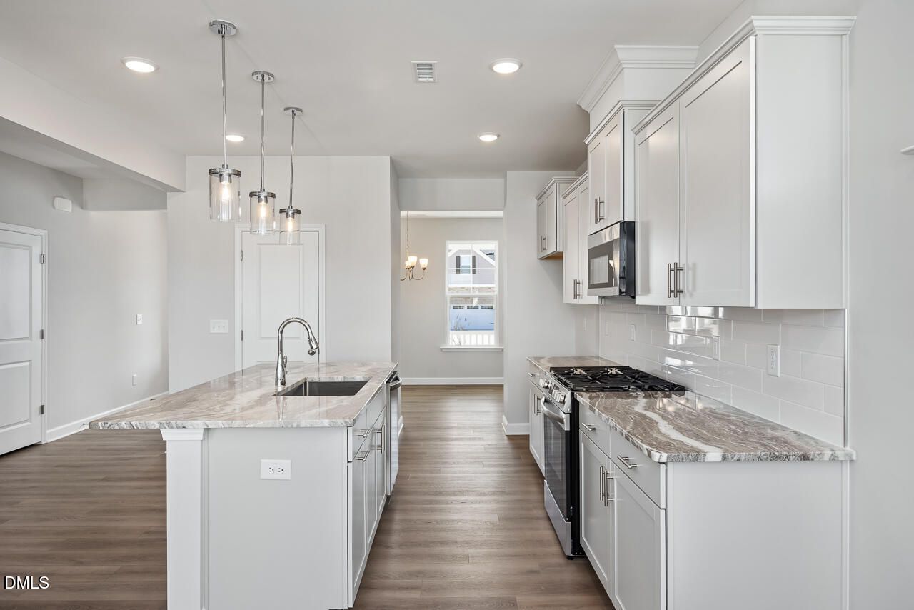 Modern kitchen featuring white cabinets, veined quartz countertops, stainless steel appliances, and central island in Davidson Homes The Willow G, Angier, NC