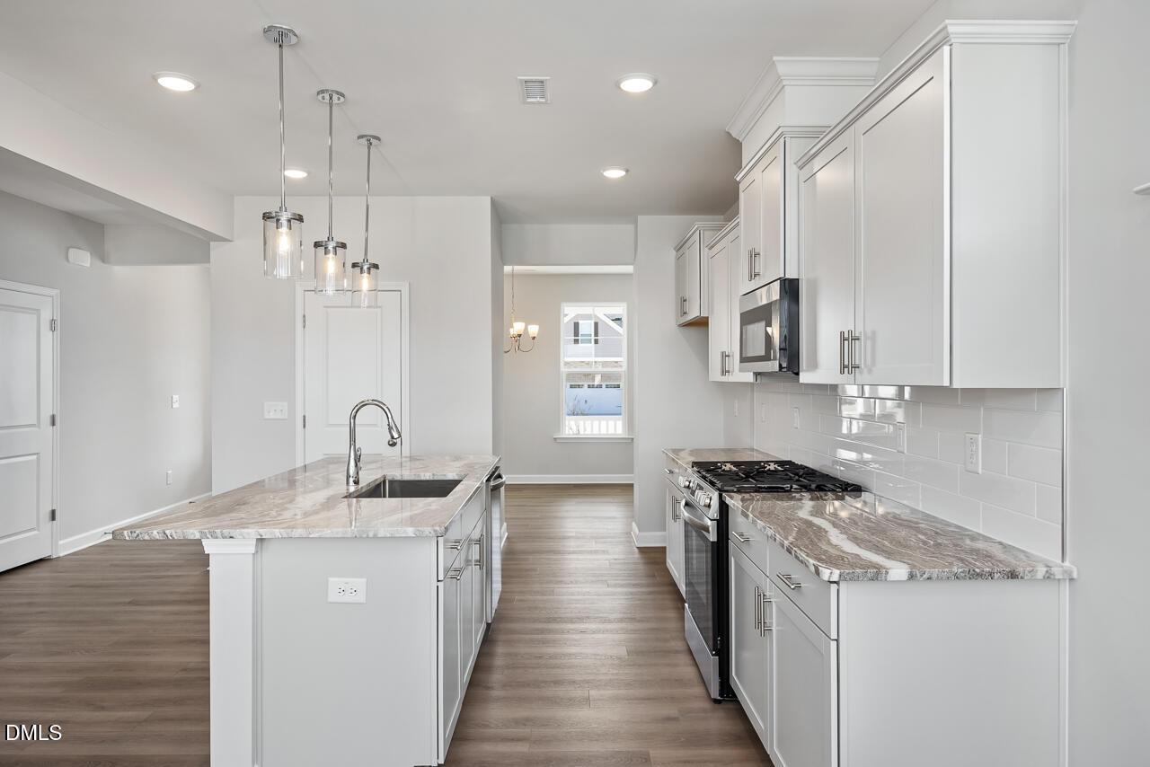 Modern kitchen featuring white cabinets, veined quartz countertops, stainless steel appliances, and central island in Davidson Homes The Willow G, Angier, NC