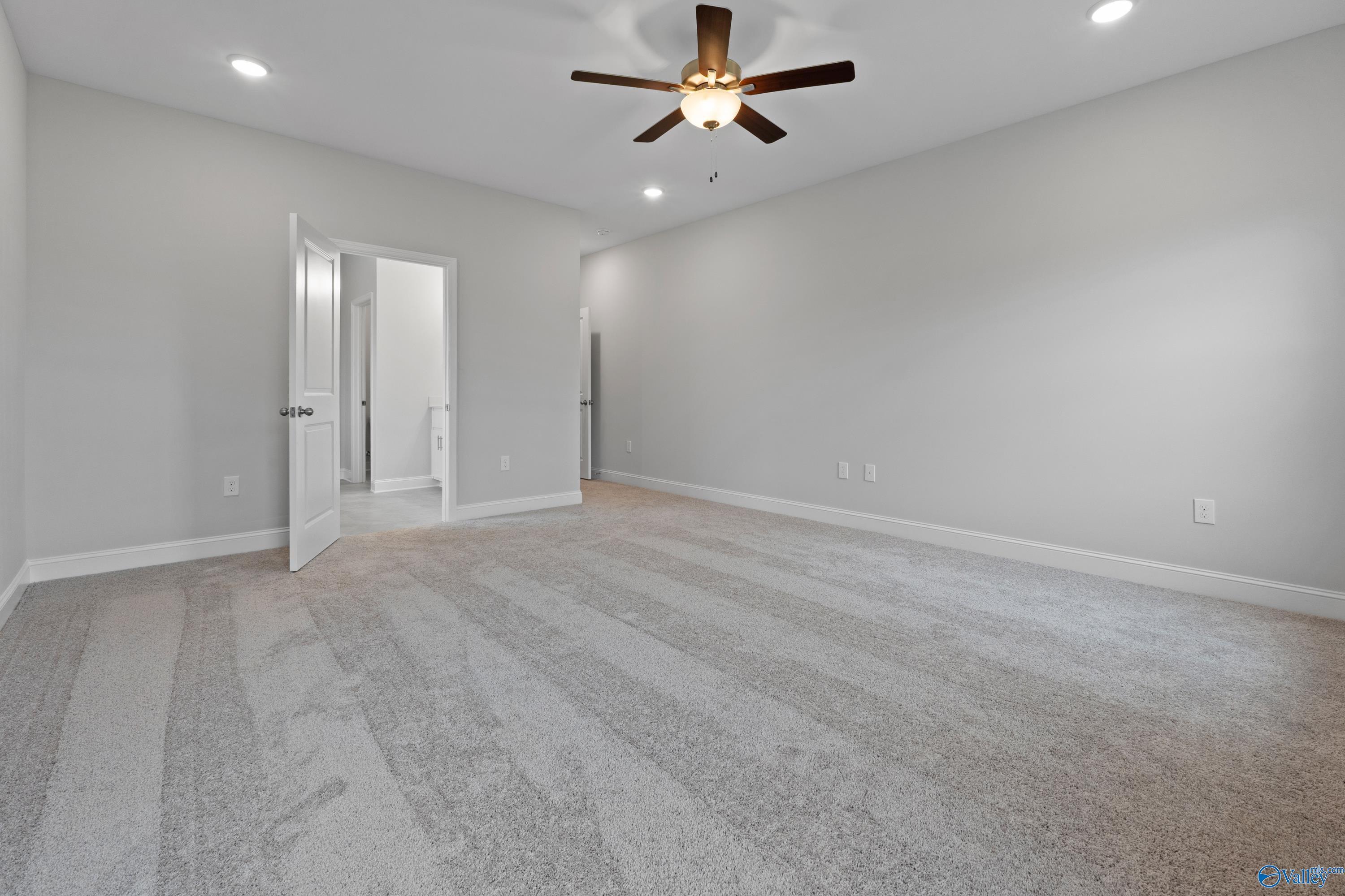 Spacious light gray bedroom with ceiling fan, recessed lights, and open door to attached bath in Davidson Homes The Rockford B, Toney, AL