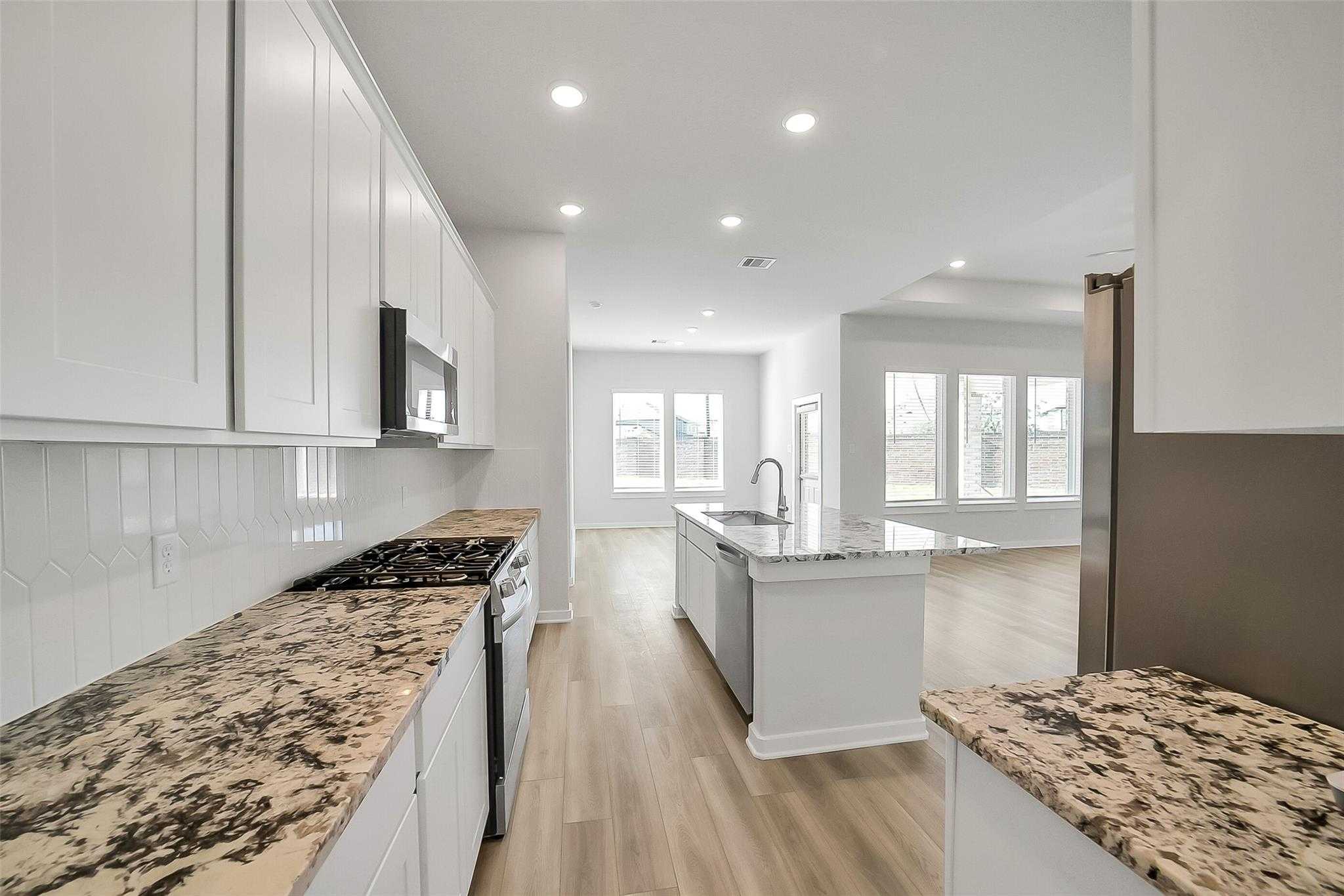 Open-concept kitchen with white shaker cabinets, speckled granite counters, stainless gas range, and island in Davidson Homes The Acadia A, Katy TX