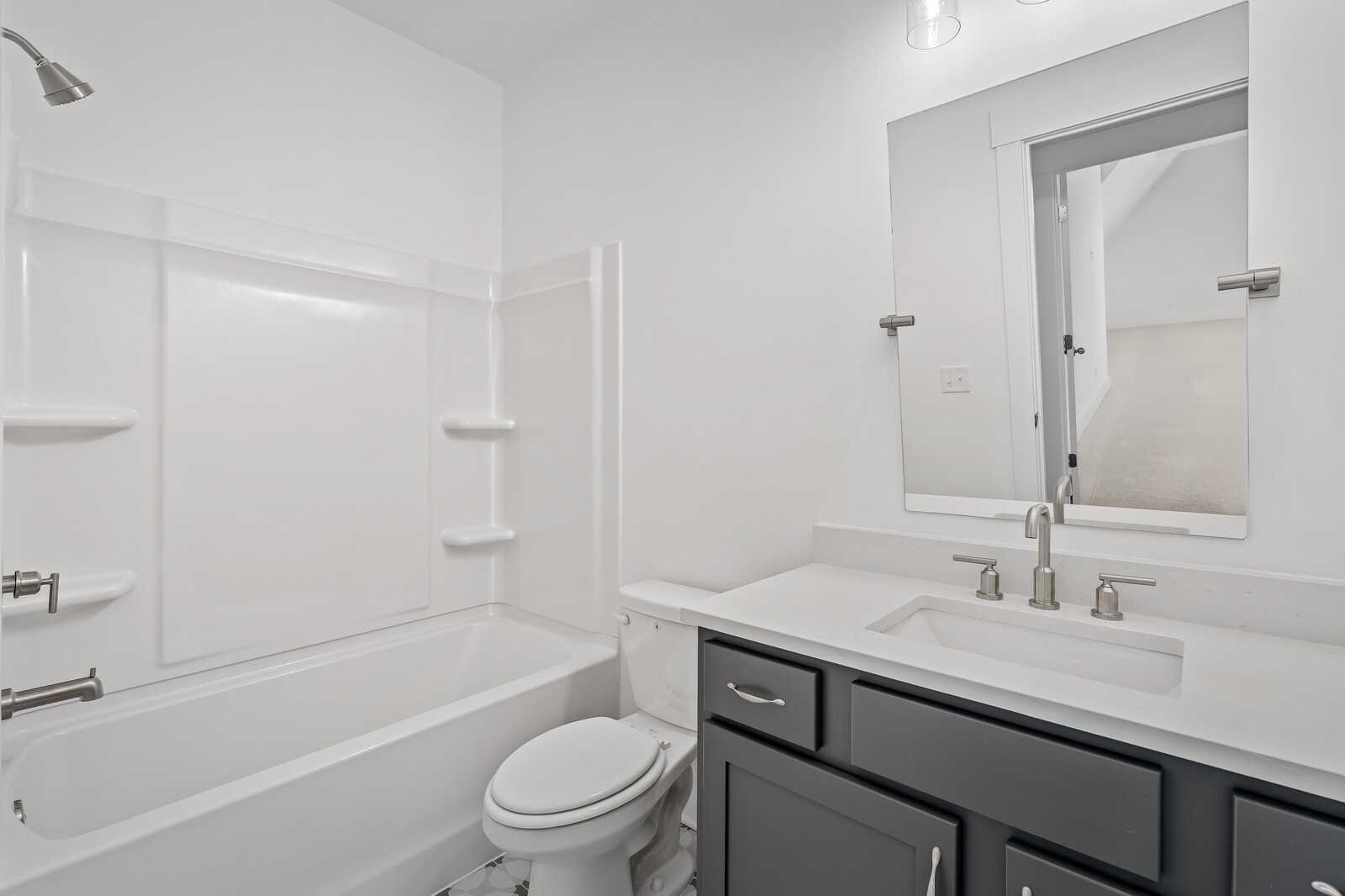 Bright bathroom with white tub-shower combo, gray vanity, single sink, and toilet in The Hawkins floor plan, Murfreesboro, Tennessee