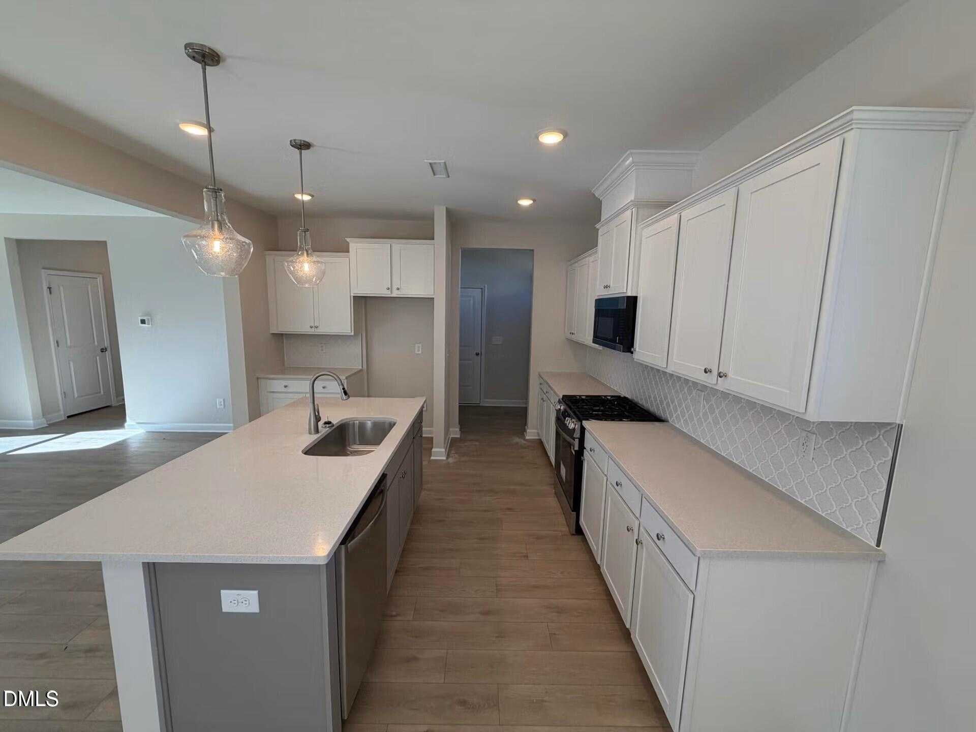 Open-concept kitchen with white shaker cabinets, quartz island sink, stainless appliances in The Gavin C home, Lillington, NC