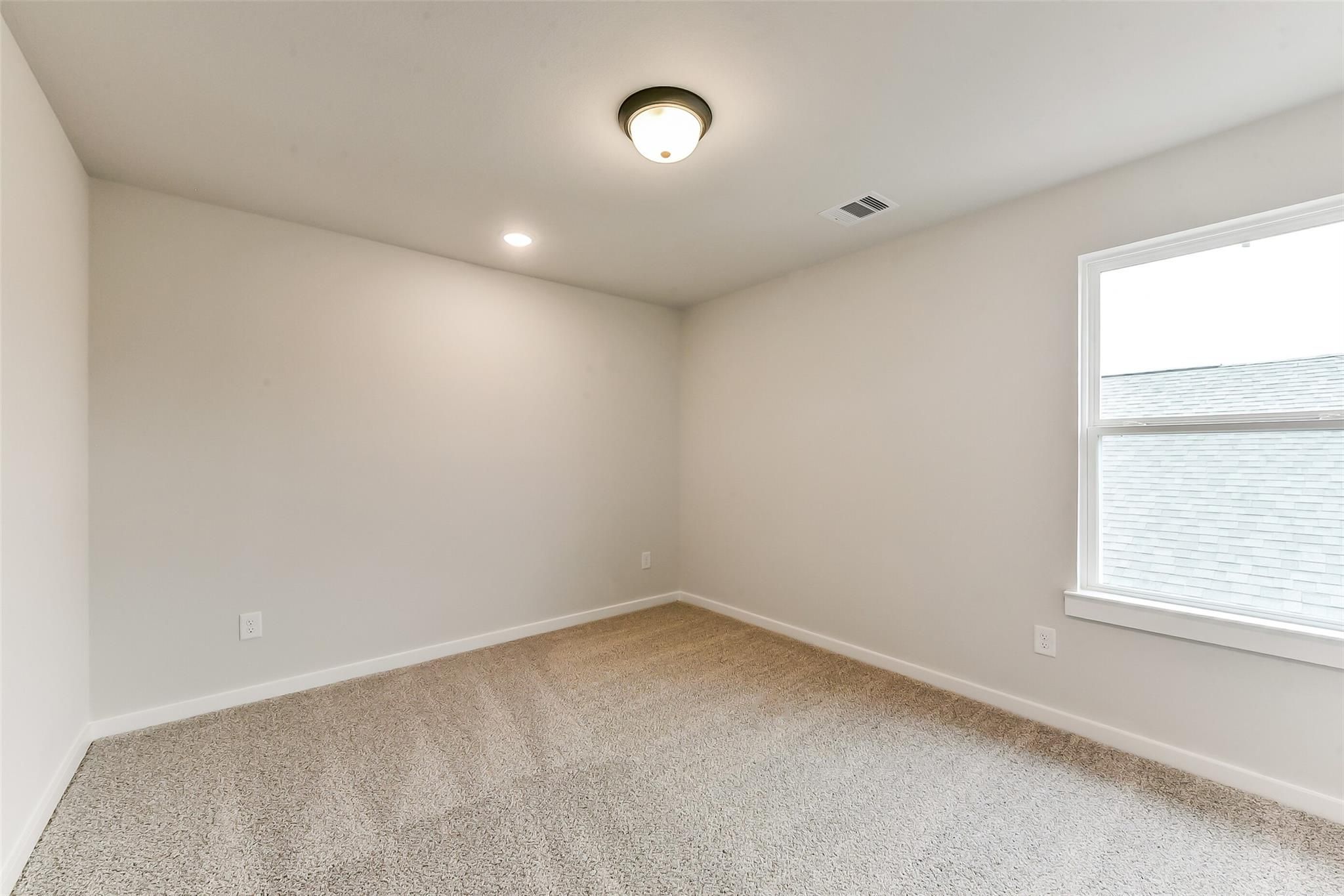 Empty bedroom with neutral beige walls, plush carpet, ceiling light, and large window in Davidson Homes Sequoia C, Crosby Texas