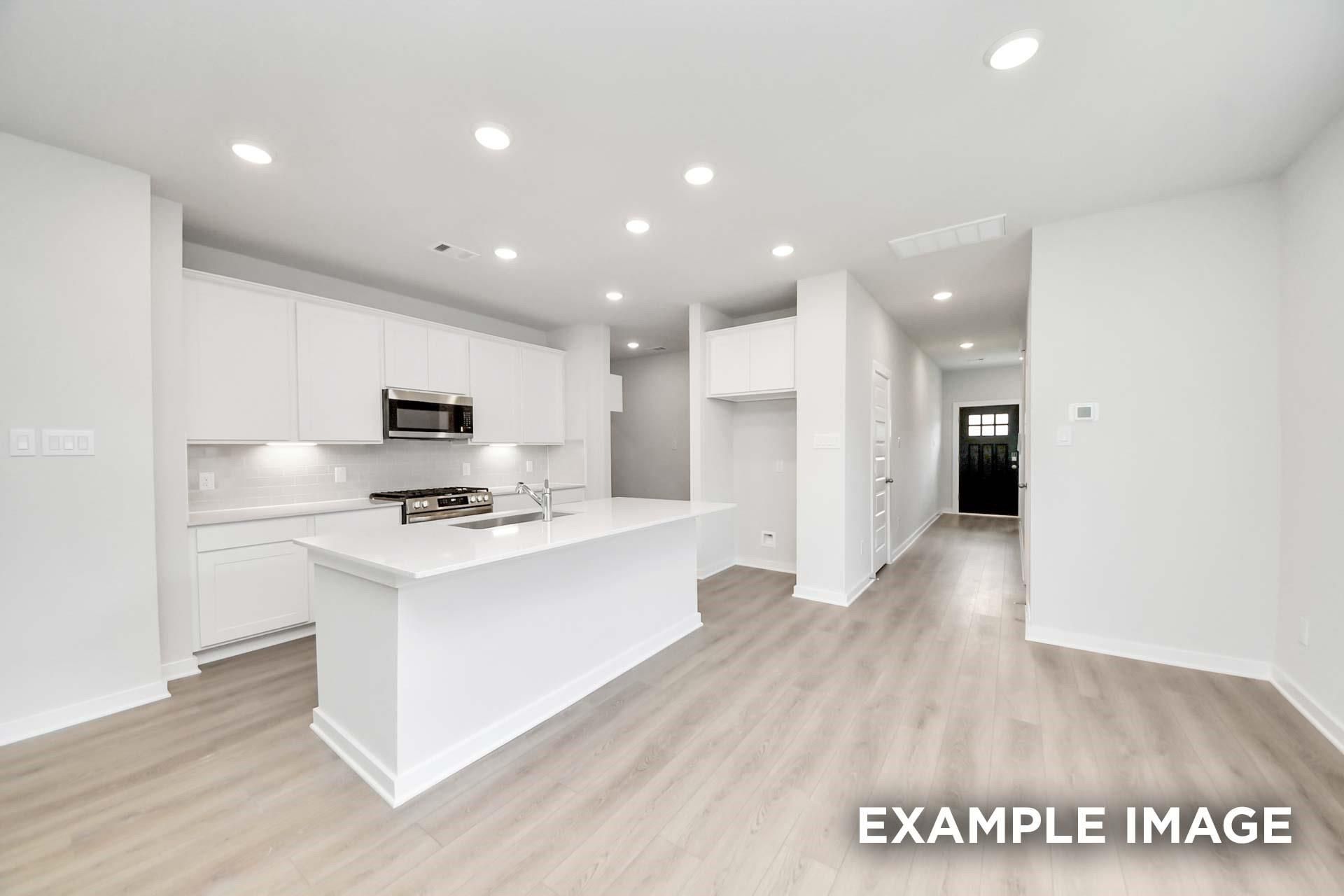 White kitchen with island, stainless appliances, and luxury vinyl plank flooring in Davidson Homes The Blanco E, Magnolia, TX