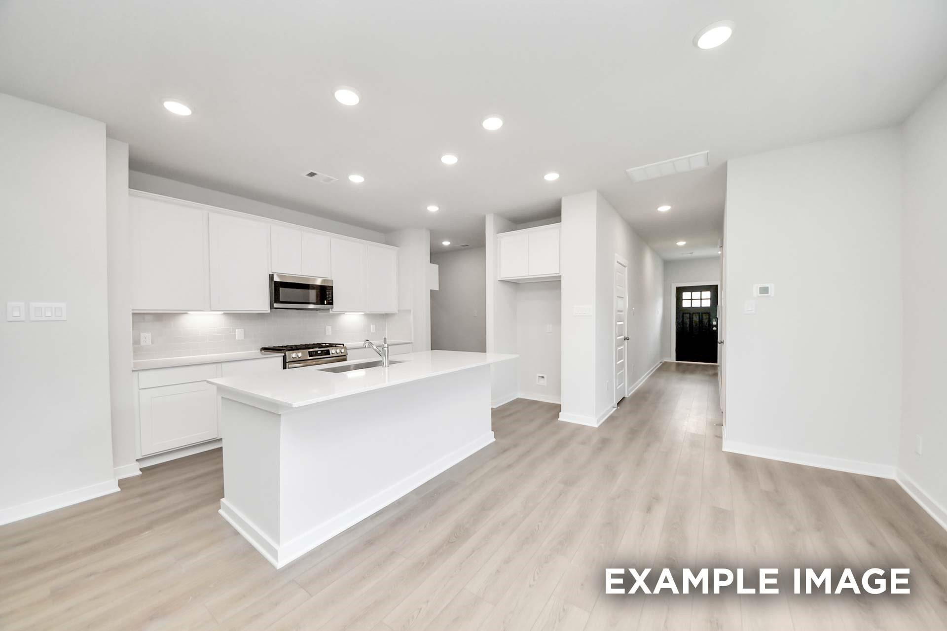 White kitchen with island, stainless appliances, and luxury vinyl plank flooring in Davidson Homes The Blanco E, Magnolia, TX