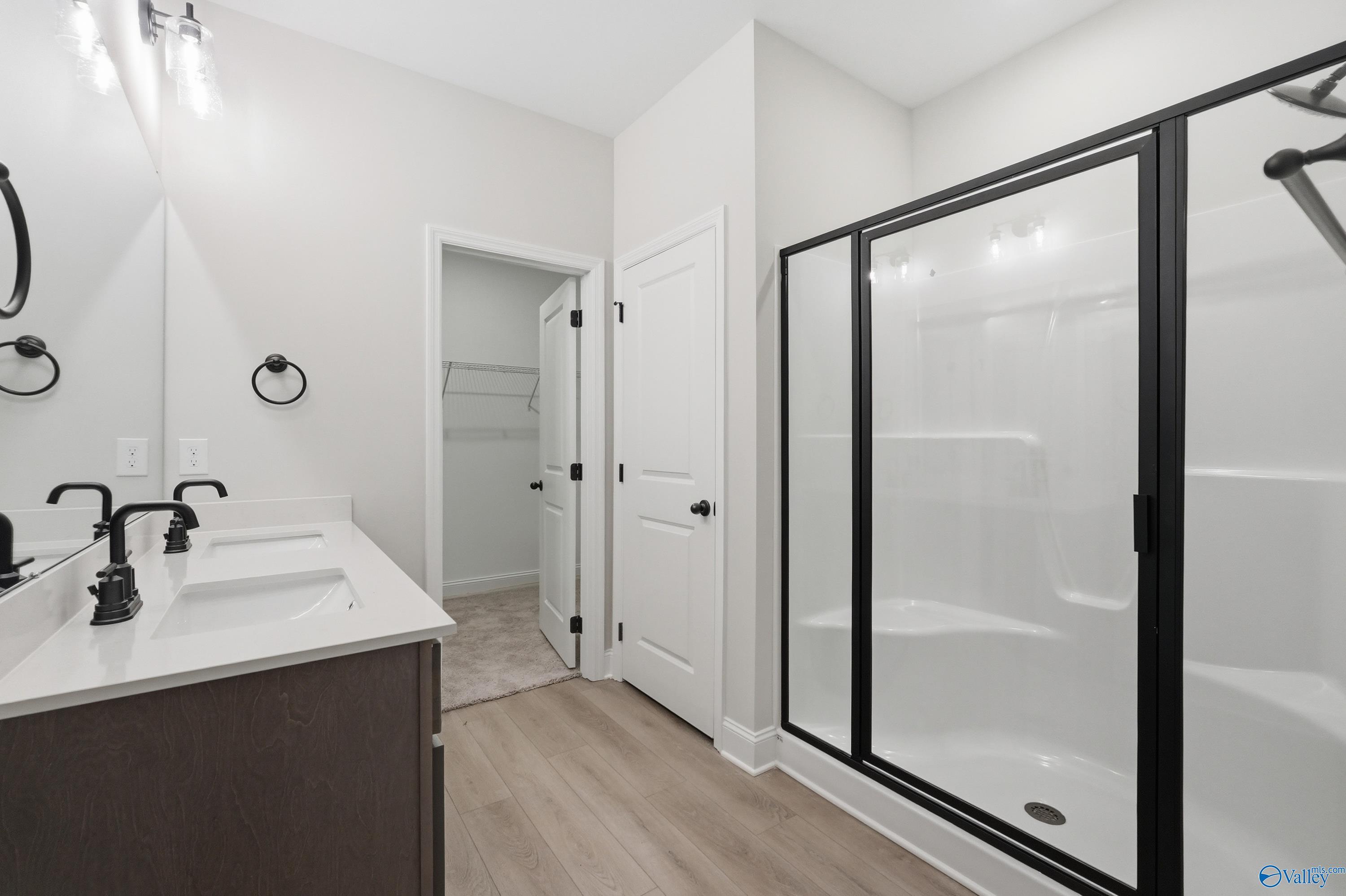 Modern master bathroom featuring double vanity with black faucets, frameless glass shower, and walk-in closet in Davidson Homes The Franklin, Huntsville AL