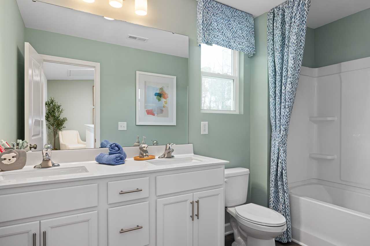 Spacious bathroom at Gregory Village Townhomes in Lillington NC with mint green walls, double vanity, blue curtains, and tub shower combo