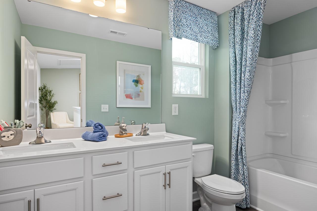 Spacious bathroom at Gregory Village Townhomes in Lillington NC with mint green walls, double vanity, blue curtains, and tub shower combo