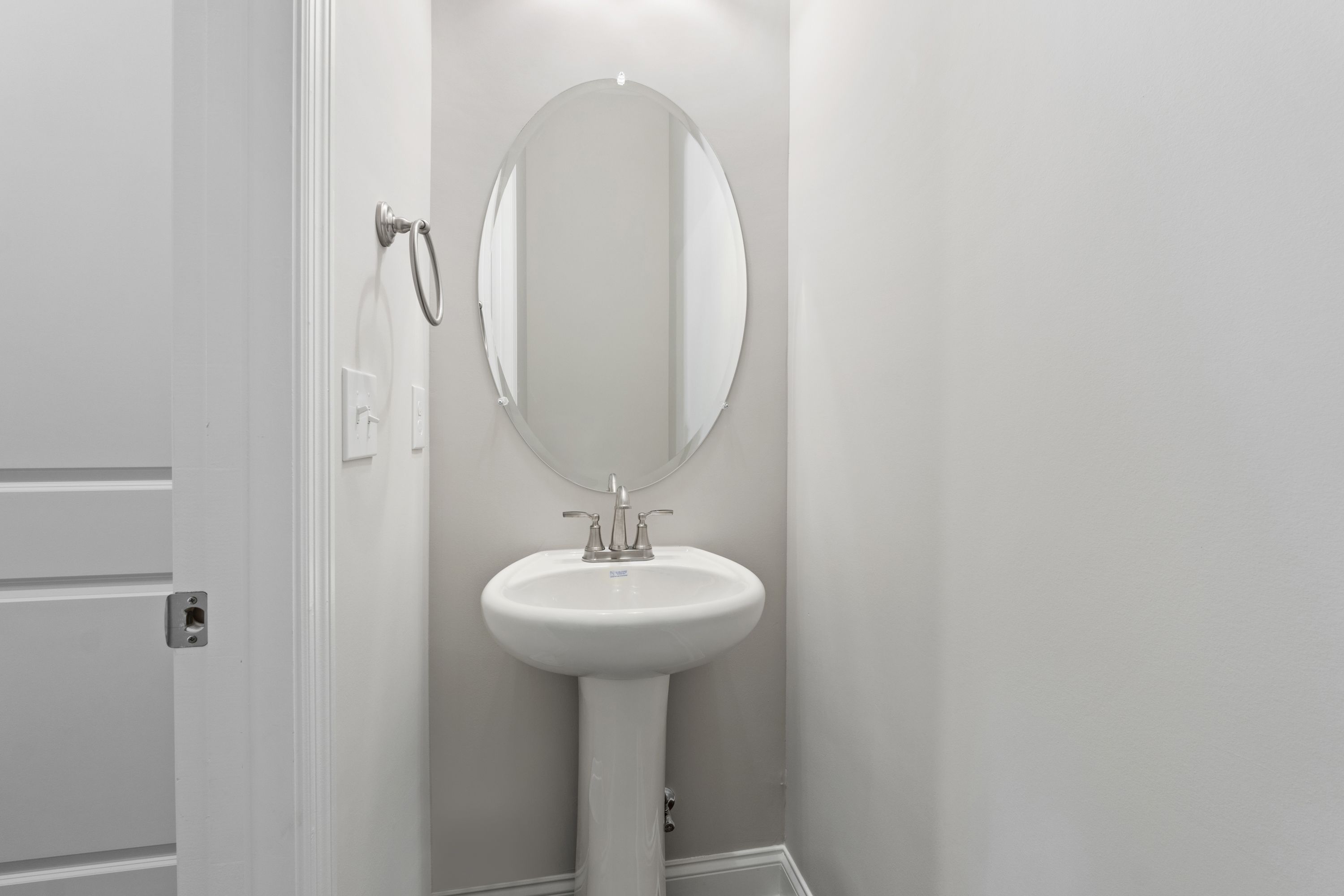 Modern powder room in The Haven D with white pedestal sink, round mirror, and chrome fixtures by Evermore Homes