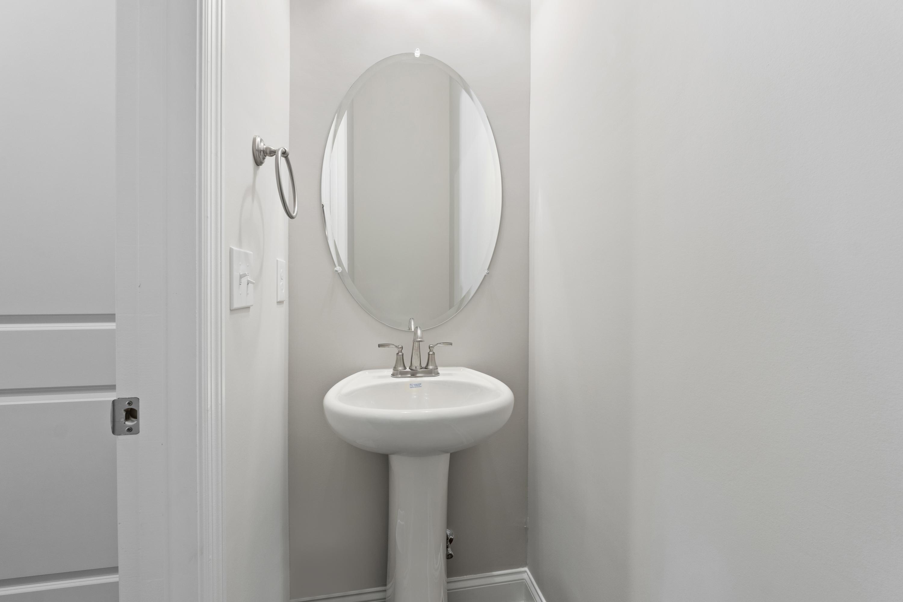 Modern powder room in The Haven D with white pedestal sink, round mirror, and chrome fixtures by Evermore Homes