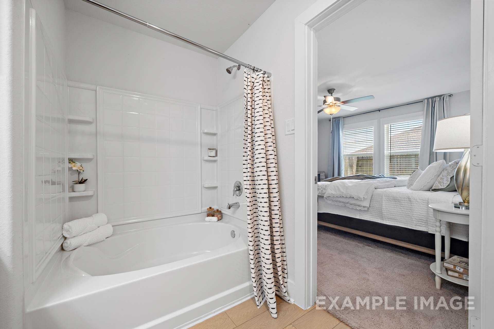 Master bathroom in The Rose B Davidson Homes design, Cypress TX, featuring white soaking tub, shower, open to upstairs bedroom suite with bed and fan