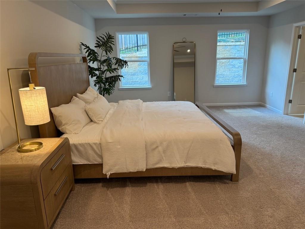 Spacious master bedroom with wooden king bed, nightstand lamp, potted plant, and large windows in Davidson Homes The Cary A, Kennesaw, Georgia