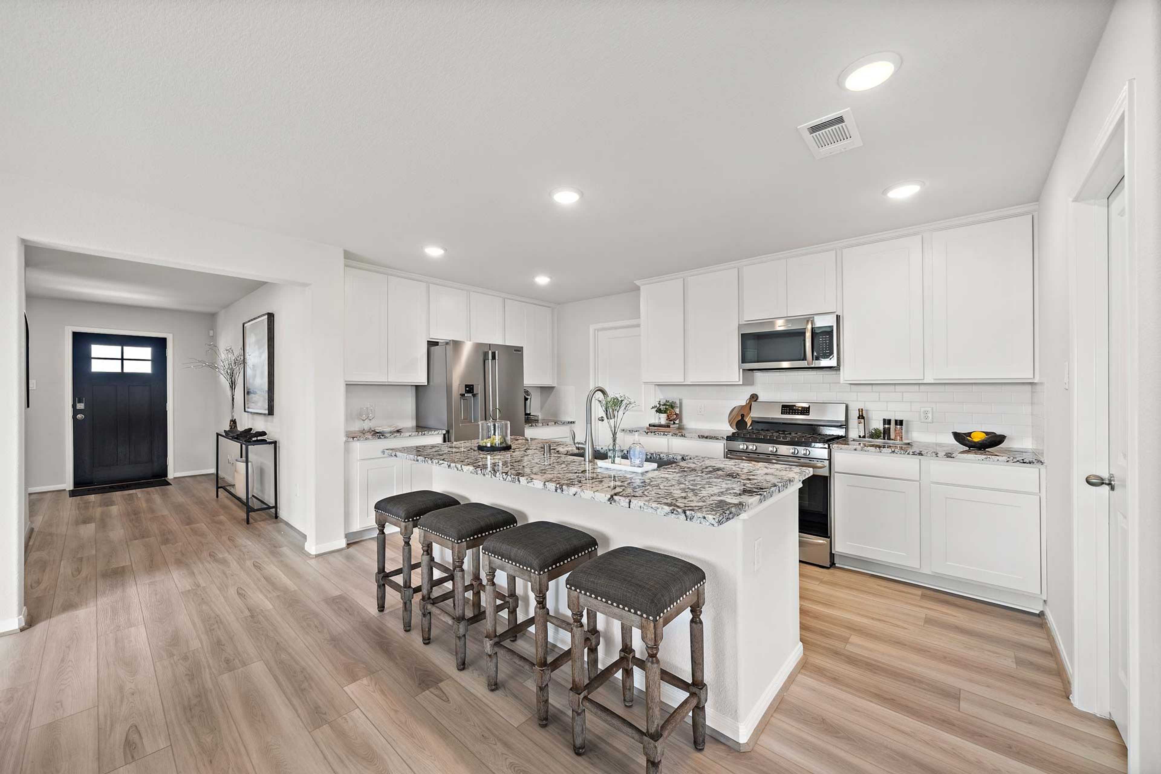Open-concept kitchen at Enclave at Newport in Crosby Texas with white cabinets, granite island, bar stools, and stainless steel appliances
