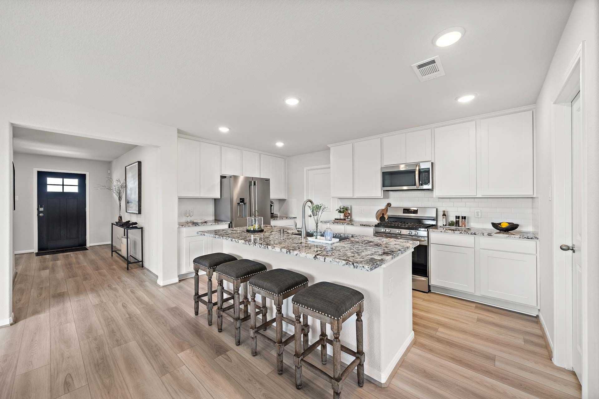 Open-concept kitchen at Enclave at Newport in Crosby Texas with white cabinets, granite island, bar stools, and stainless steel appliances