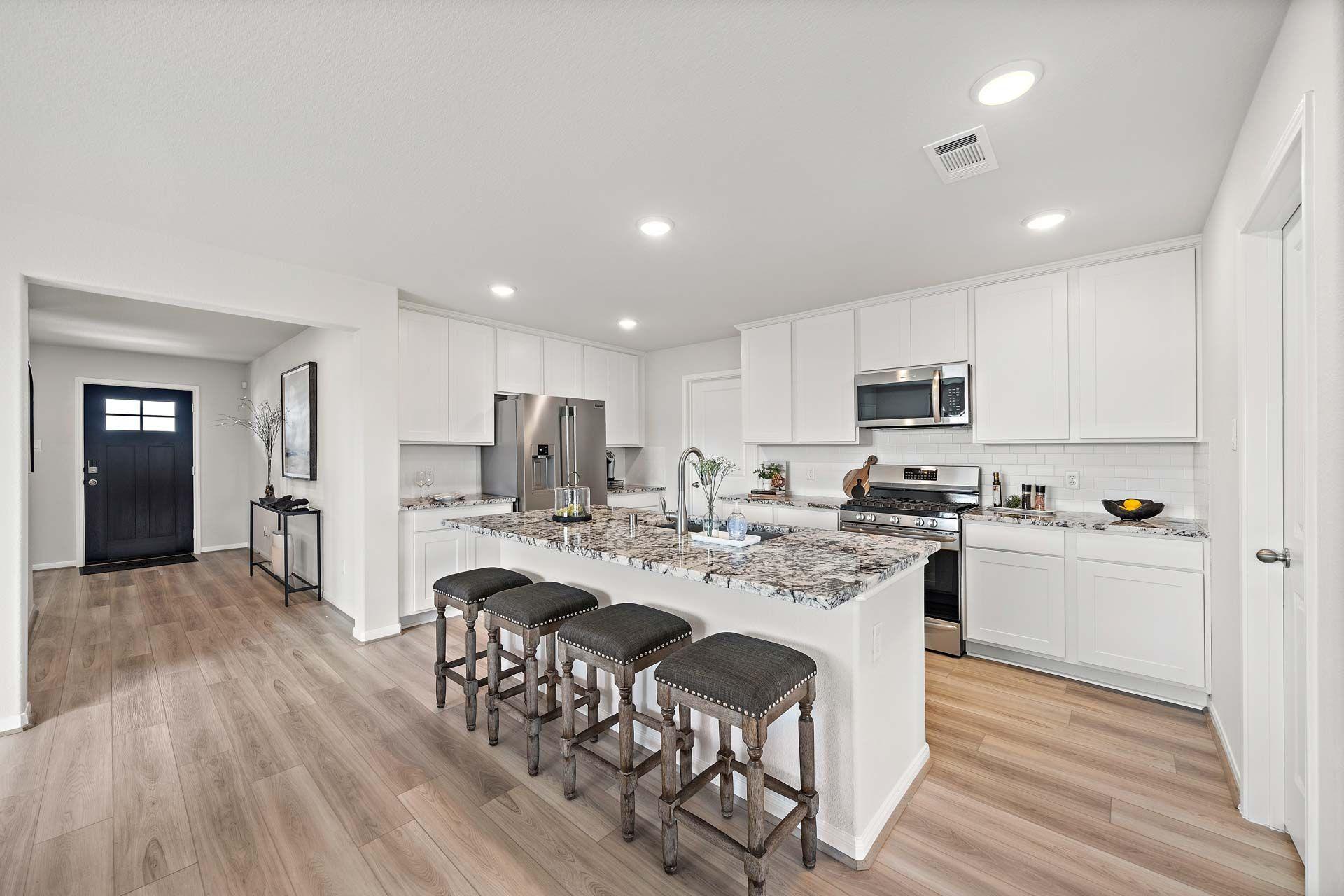 Open-concept kitchen at Enclave at Newport in Crosby Texas with white cabinets, granite island, bar stools, and stainless steel appliances