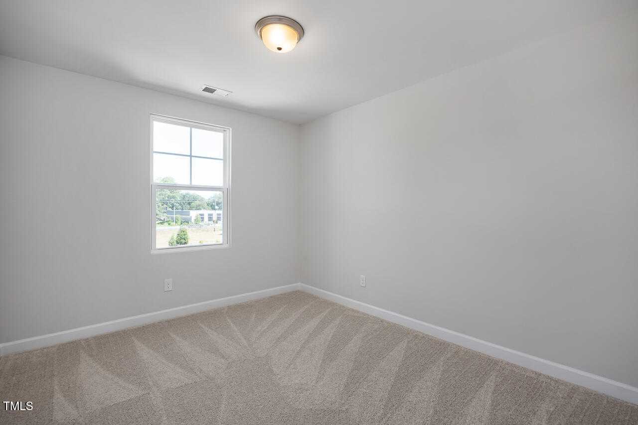 Bright secondary bedroom with neutral gray walls, beige carpet, and window view of trees in Davidson Homes The Graham, Fuquay-Varina, NC