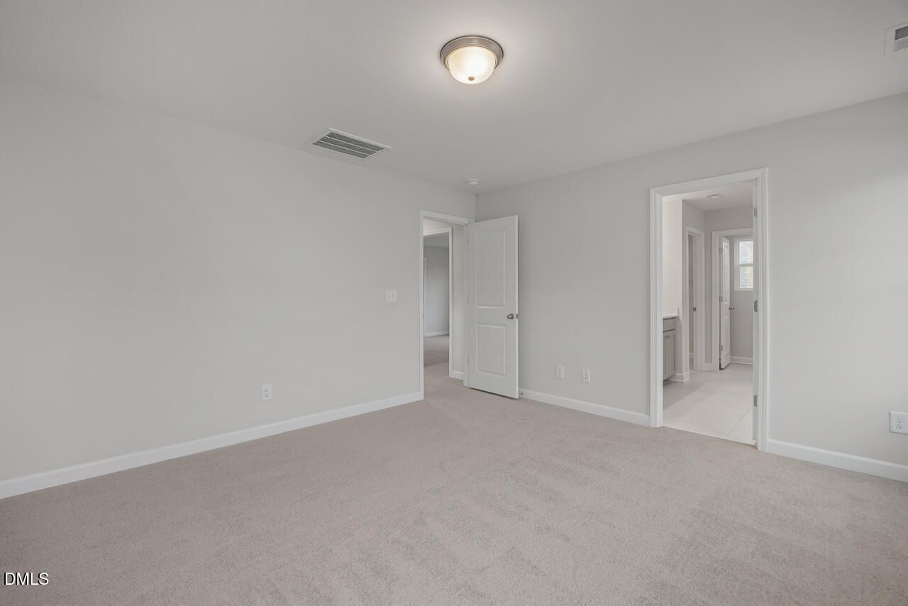 Spacious secondary bedroom with neutral walls, plush beige carpet, and en-suite bath door in Davidson Homes The Gavin B, Lillington NC