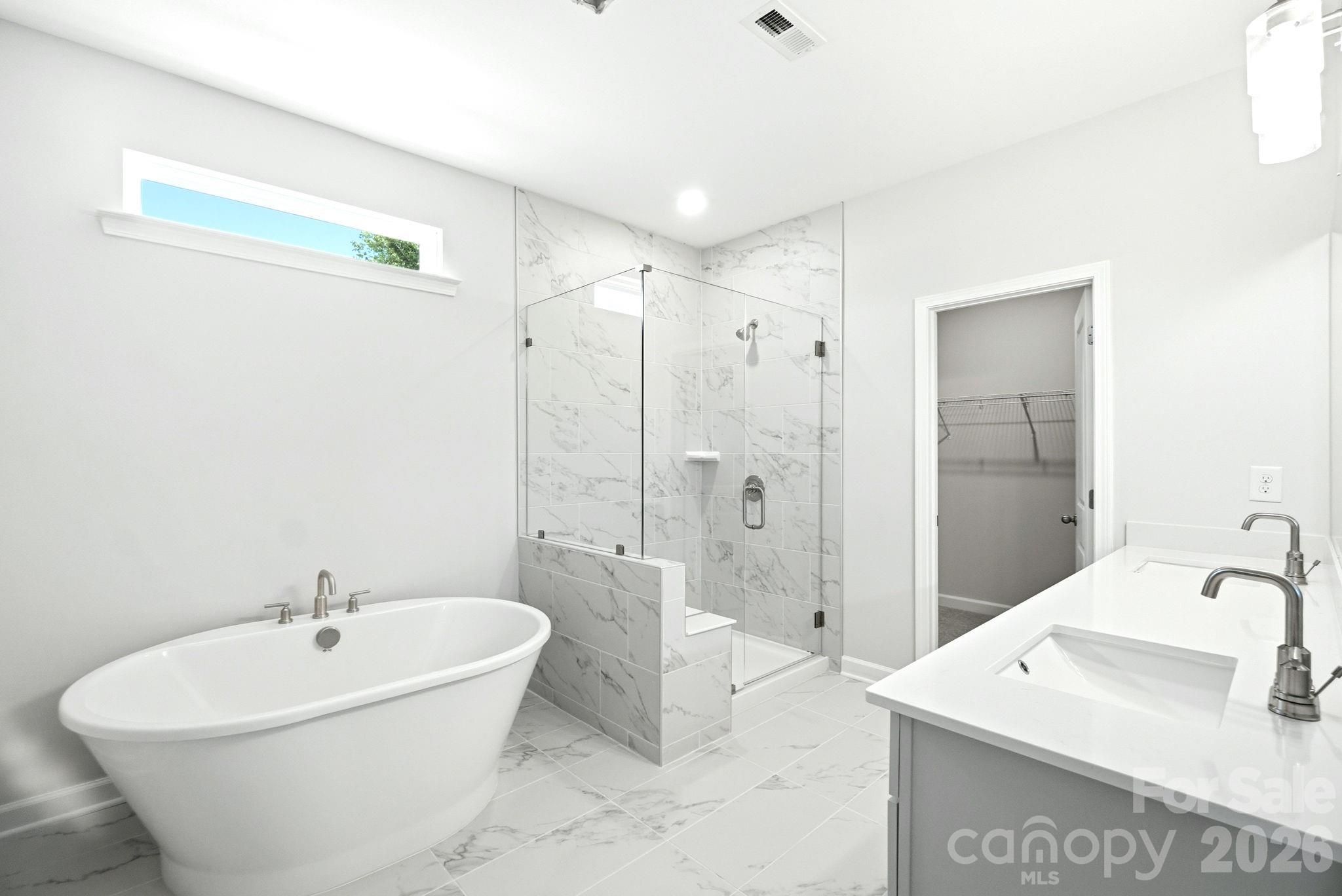 Modern master bathroom with soaking tub, marble-tiled walk-in shower, and dual vanity in Davidson Homes Magnolia B plan.