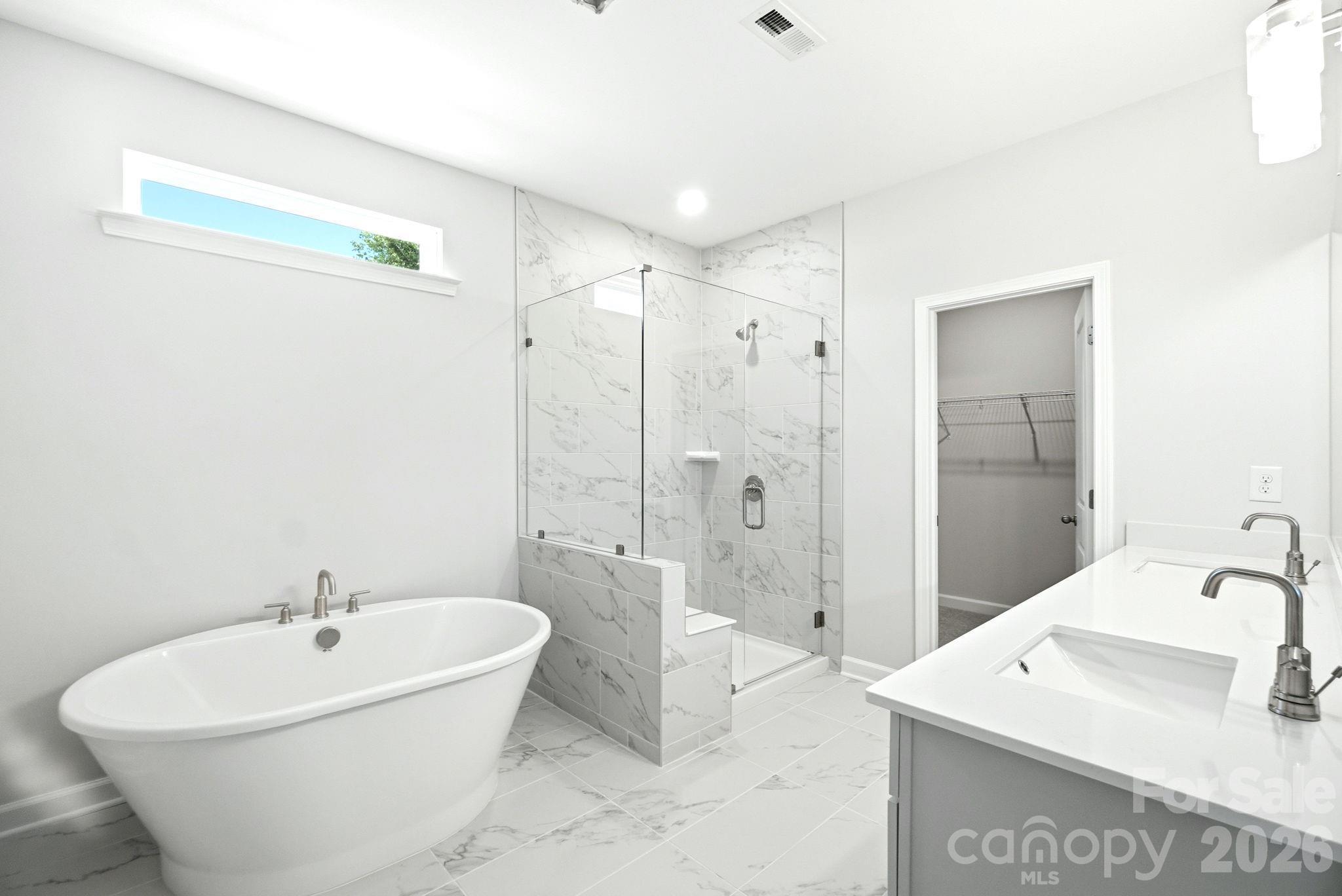 Modern master bathroom with soaking tub, marble-tiled walk-in shower, and dual vanity in Davidson Homes Magnolia B plan.
