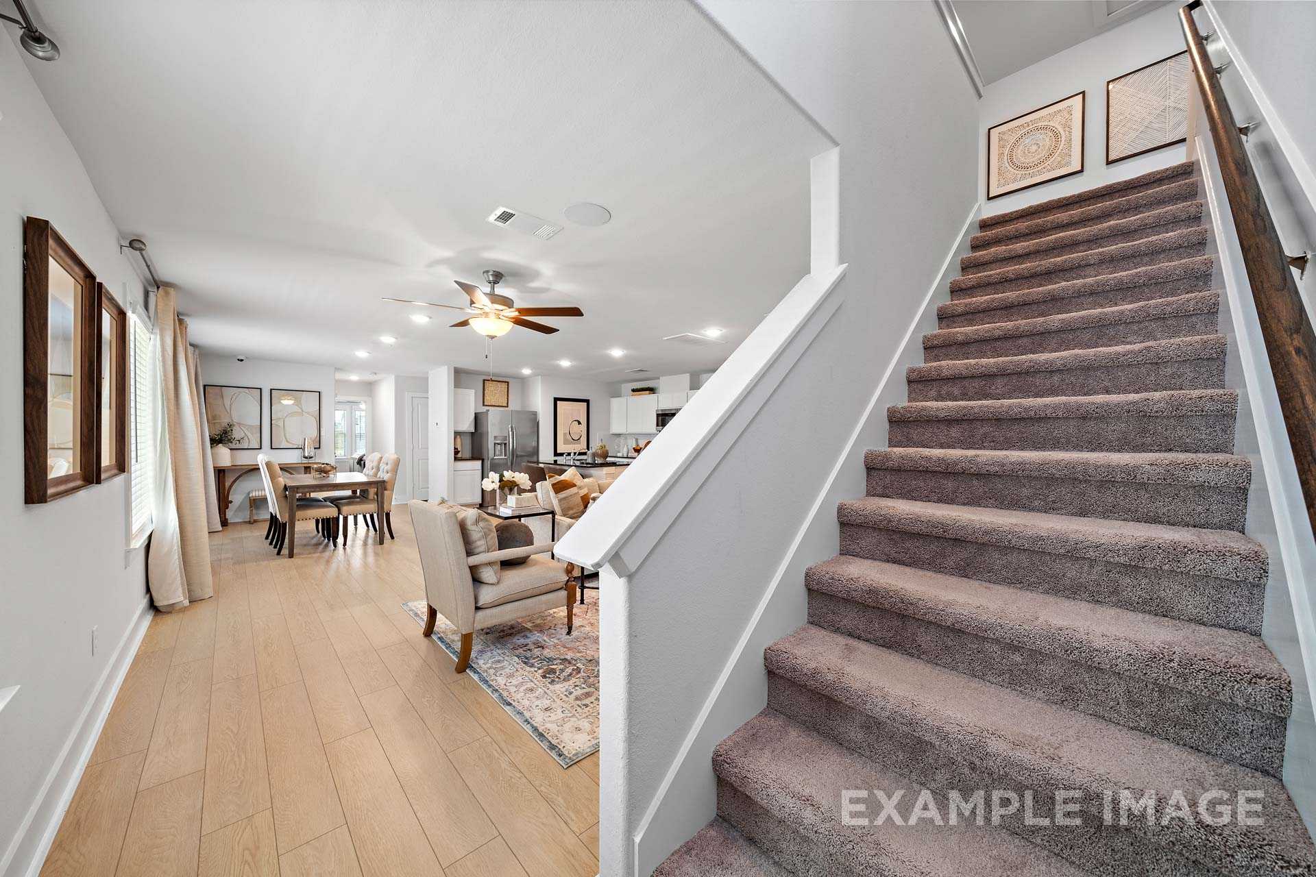 Spacious open-concept living and dining area in The Rose B with wooden floors, modern furniture, ceiling fans, and carpeted staircase to upper master suite